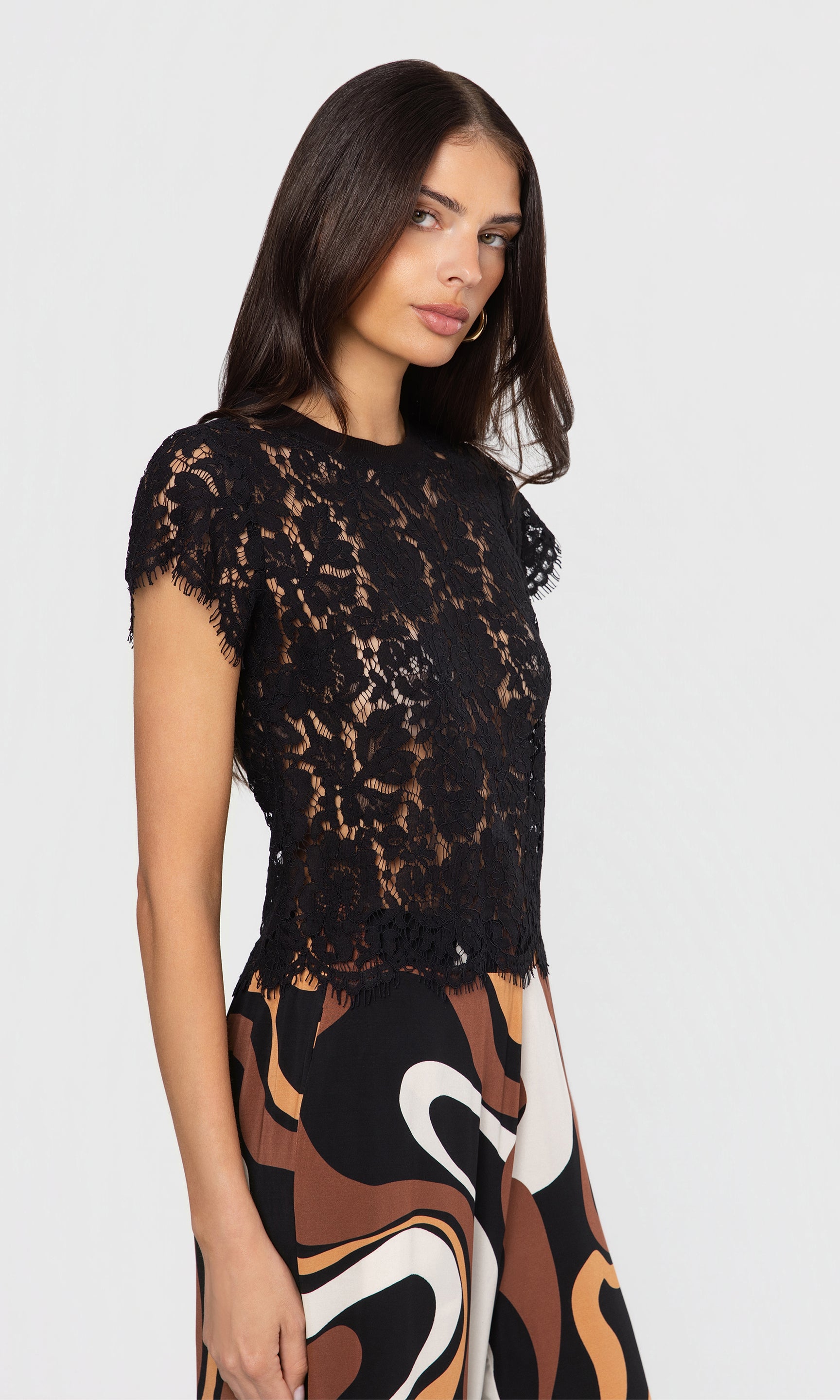 Side view of woman wearing a black lace top and patterned skirt on a white background