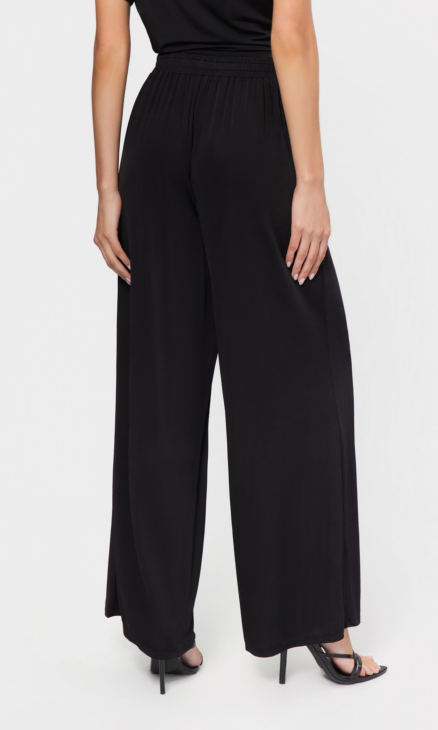 Back view of person wearing a black outfit with wide-leg pants on a white background