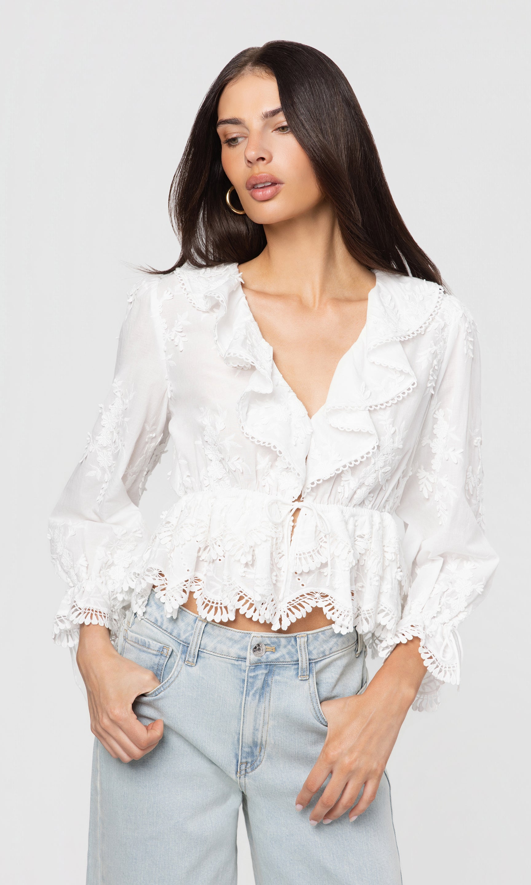 Side view of woman wearing a white lace top and light blue jeans against a plain background