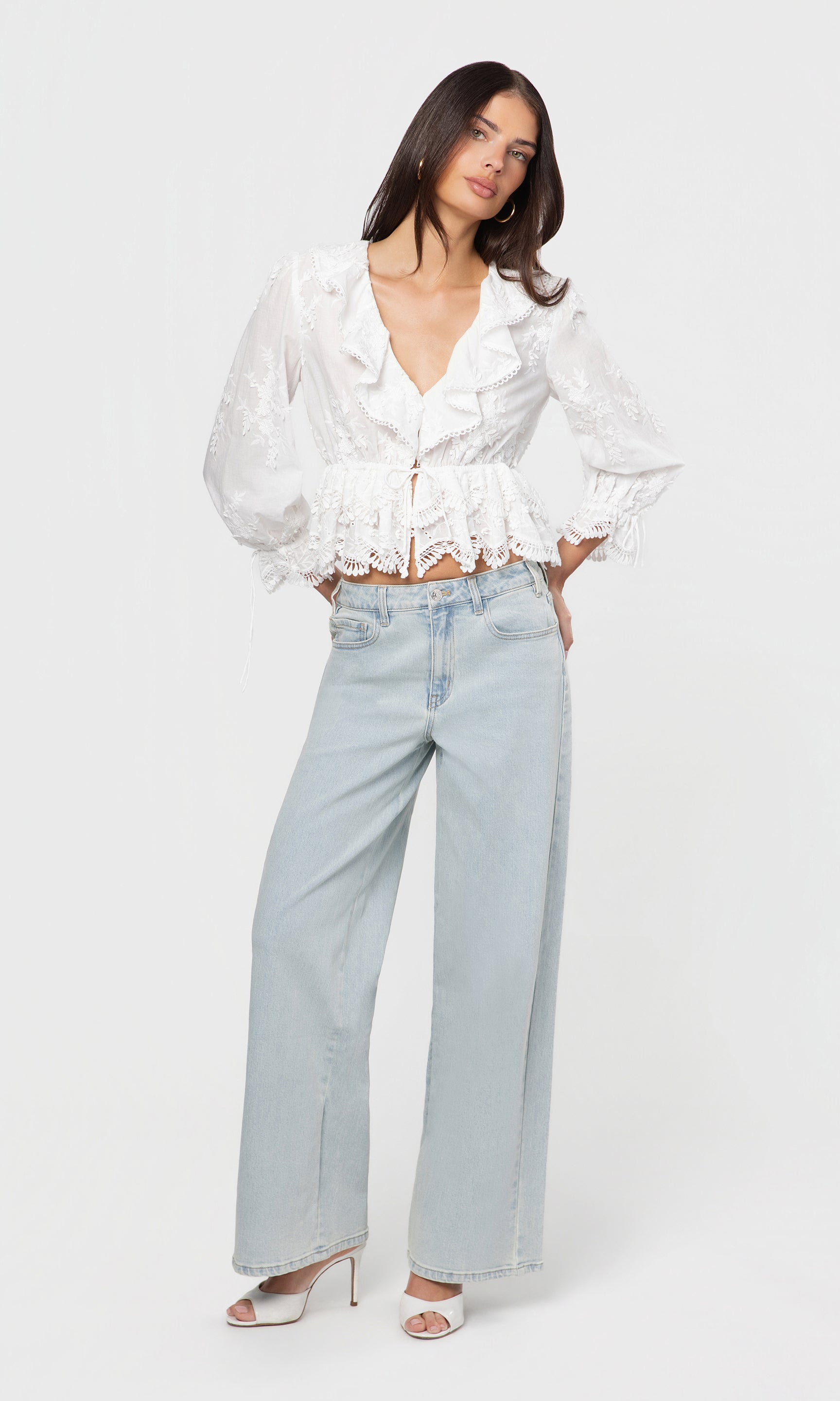 Woman wearing a white blouse with ruffles and light blue jeans on a white background