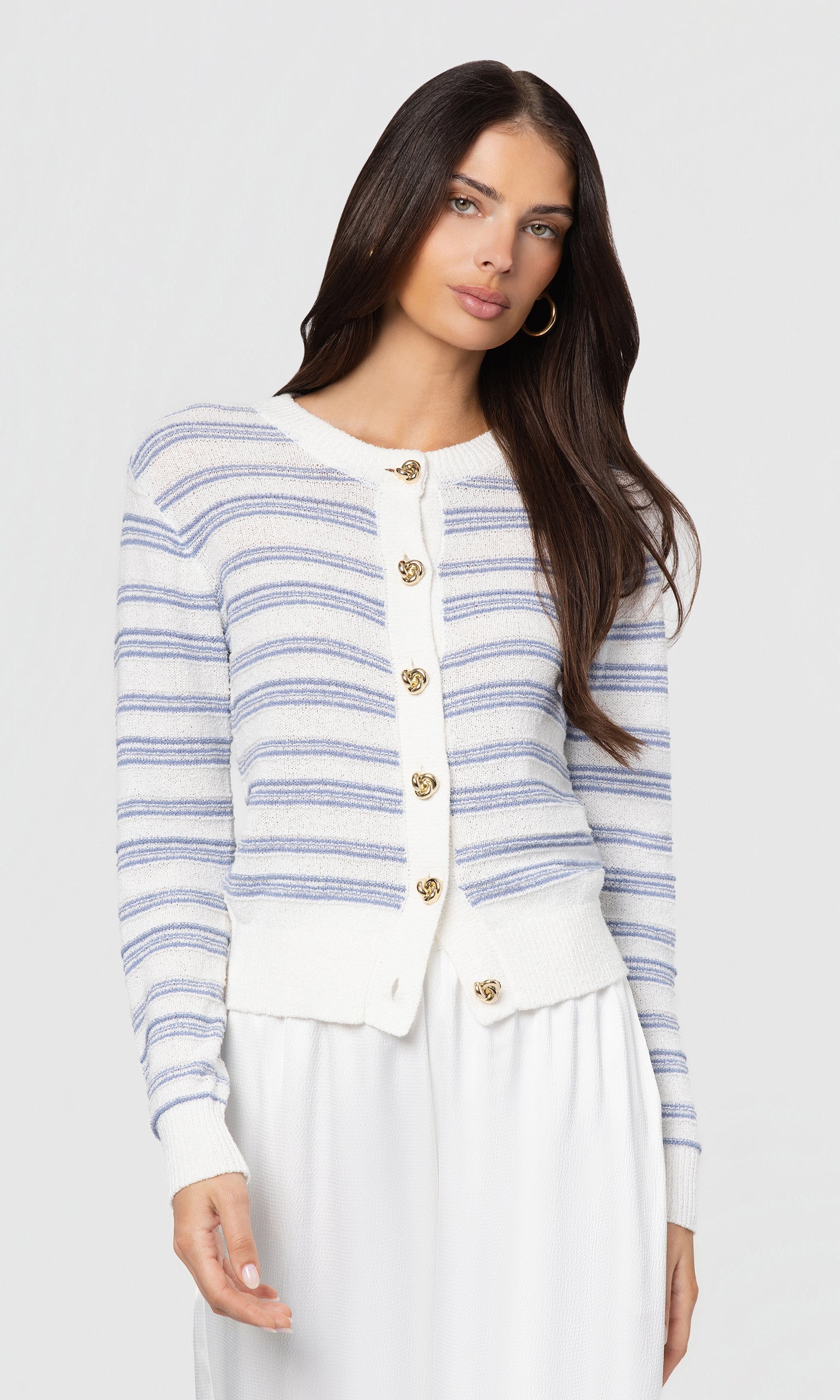 Woman wearing a striped cardigan with gold buttons on a plain background