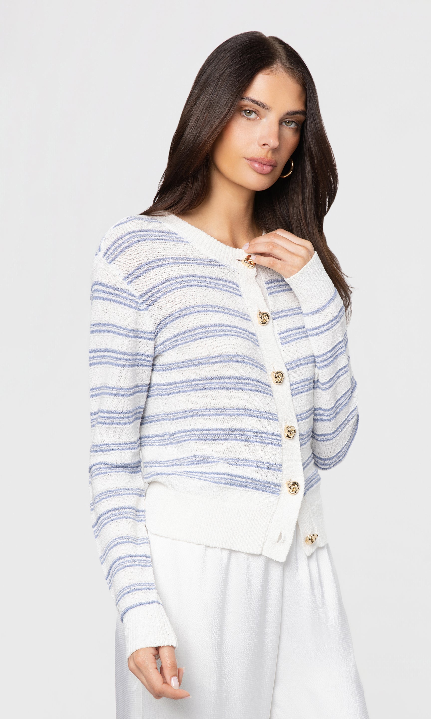 Side view of woman wearing a striped cardigan with gold buttons on a plain background