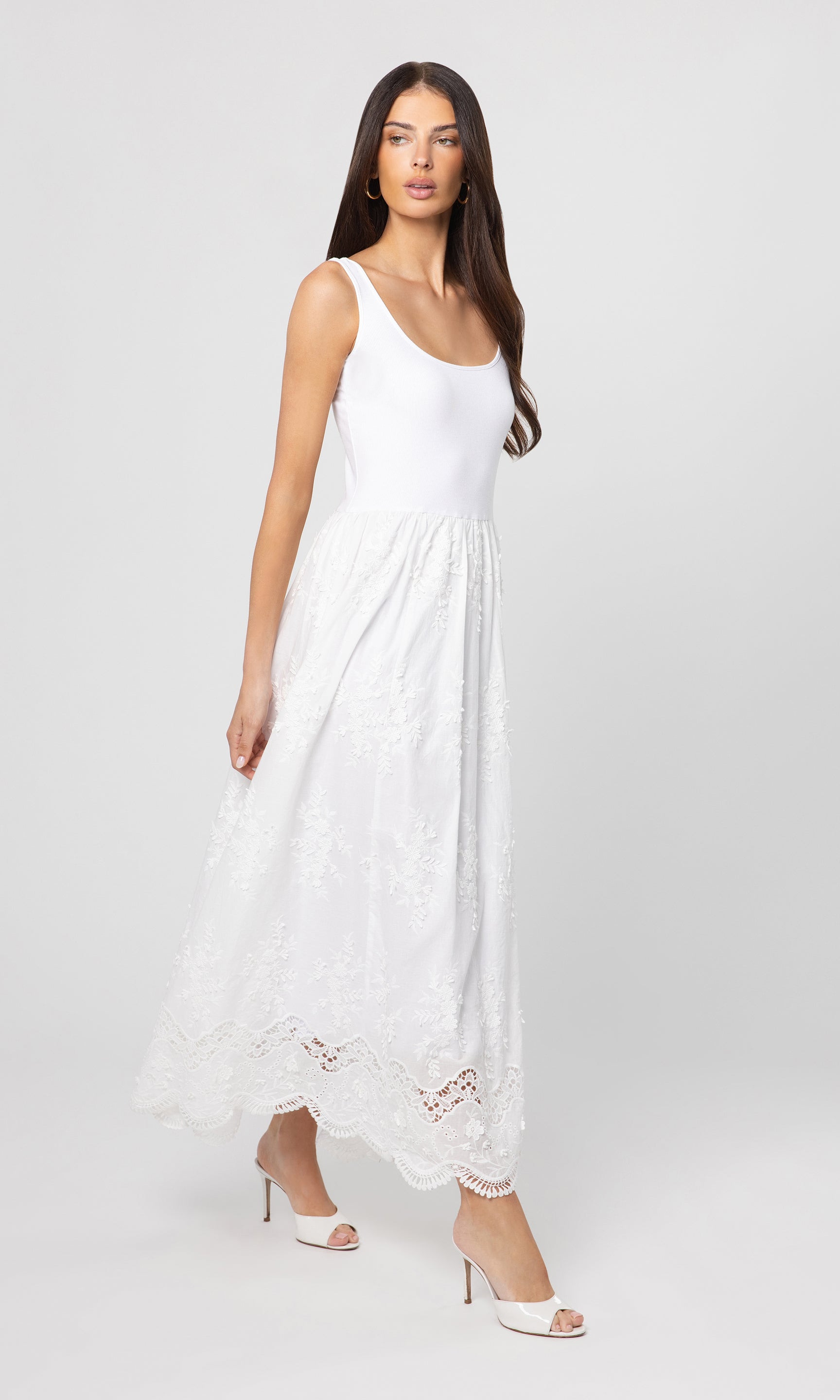 Side view of woman wearing a white sleeveless dress with lace details on a white background