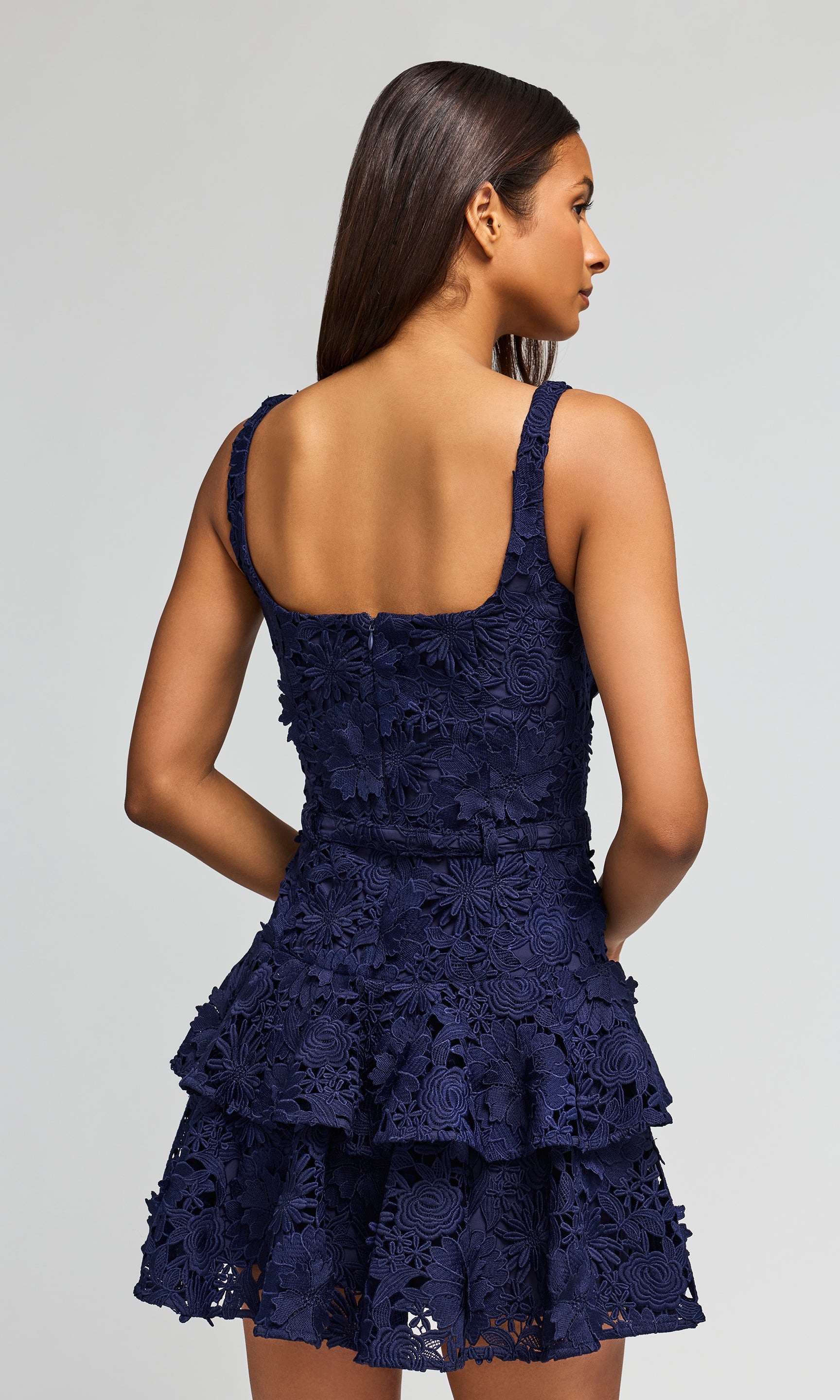 Back view of navy lace dress worn by a model on a gray background