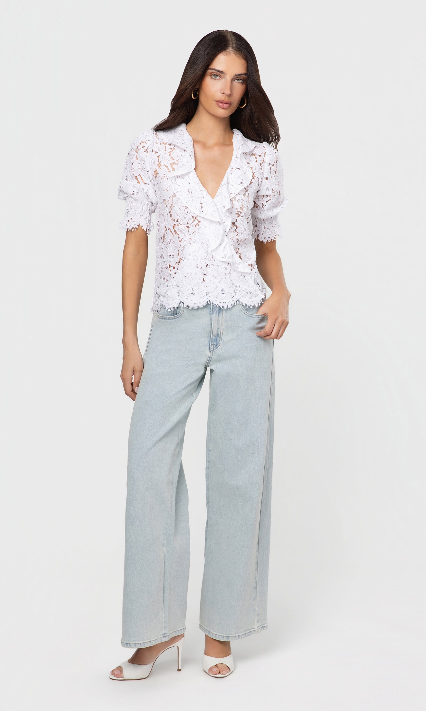 Woman wearing a white lace blouse and light blue jeans on a white background