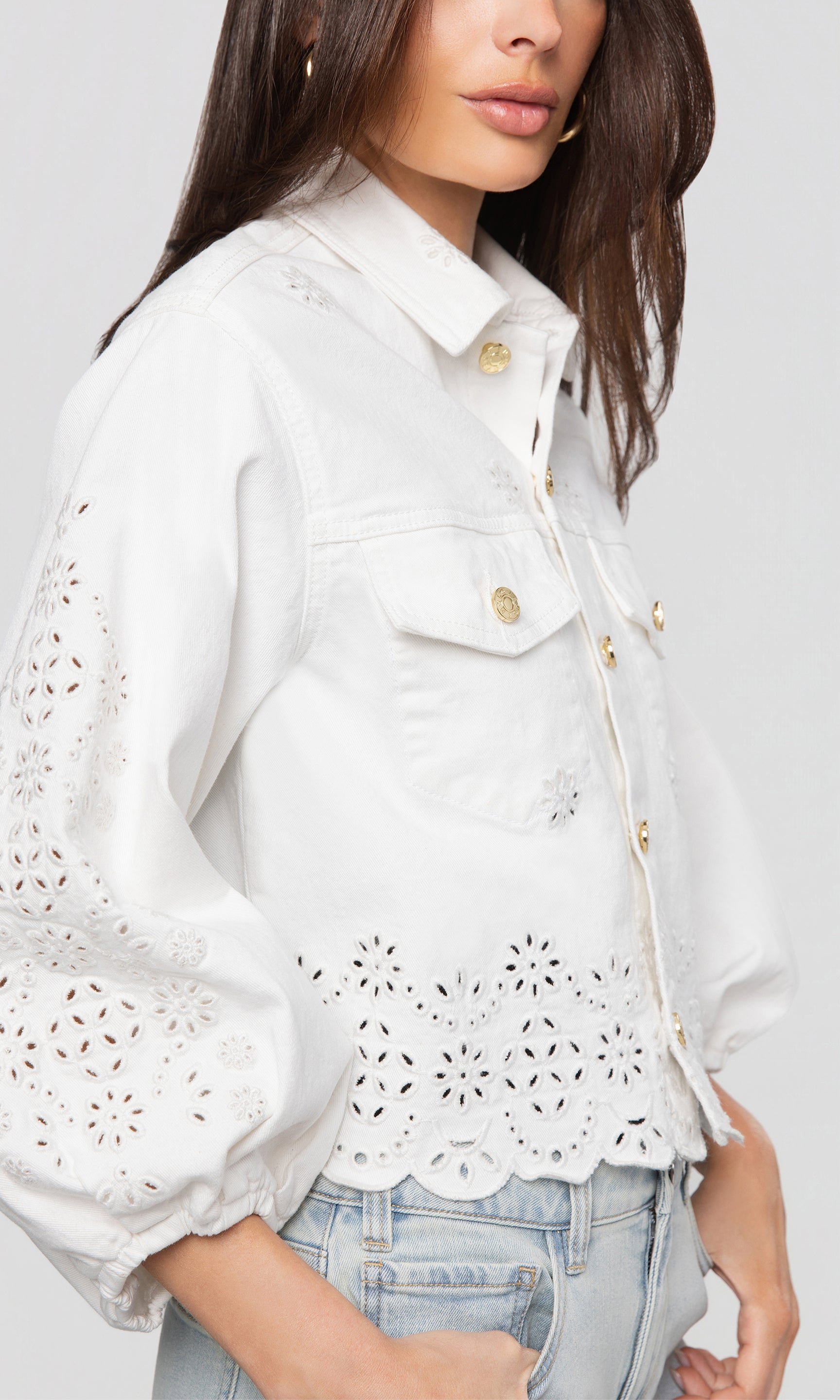 Close-up of white denim jacket with lace detailing worn by a person on a plain background