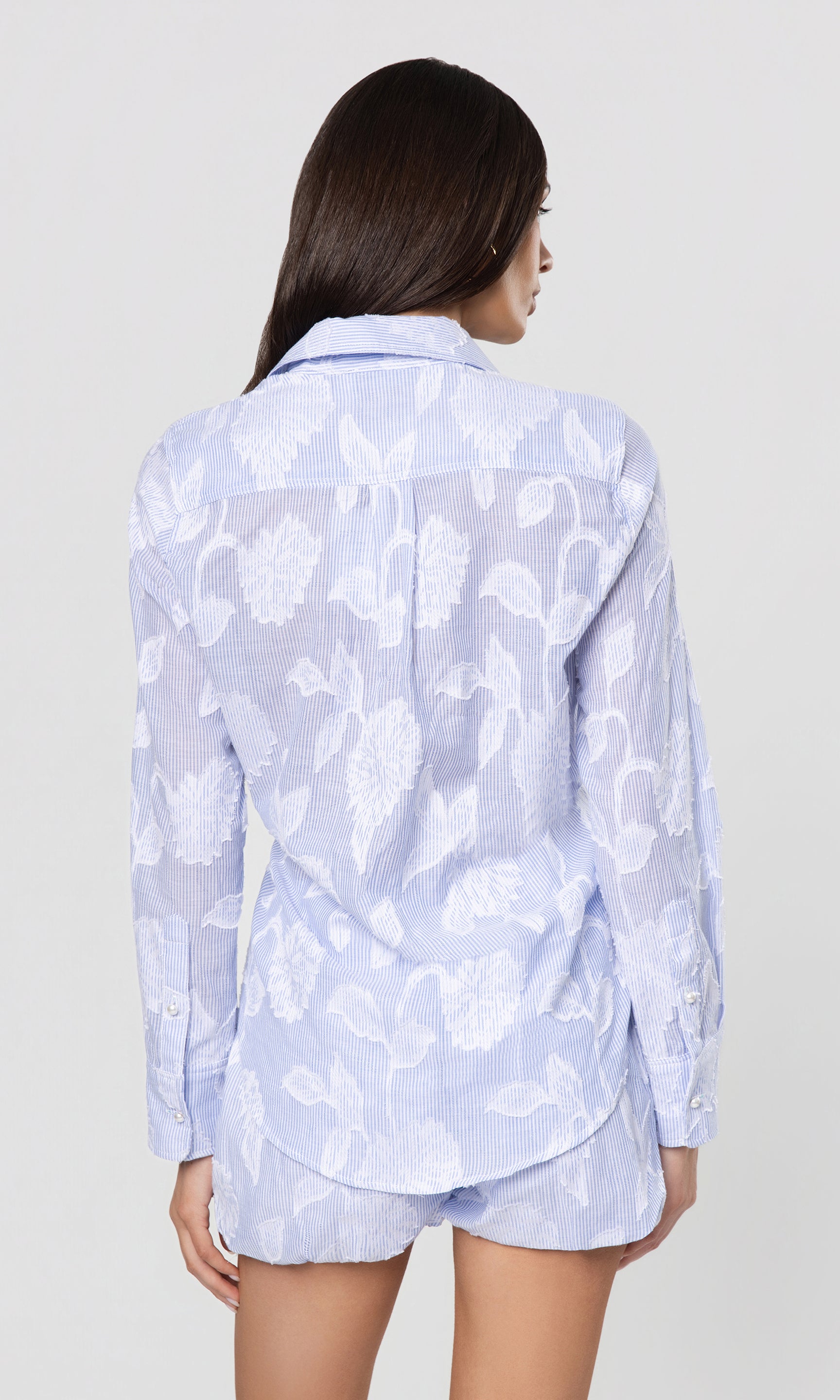 Back view of woman wearing a light blue floral pajama set on a white background