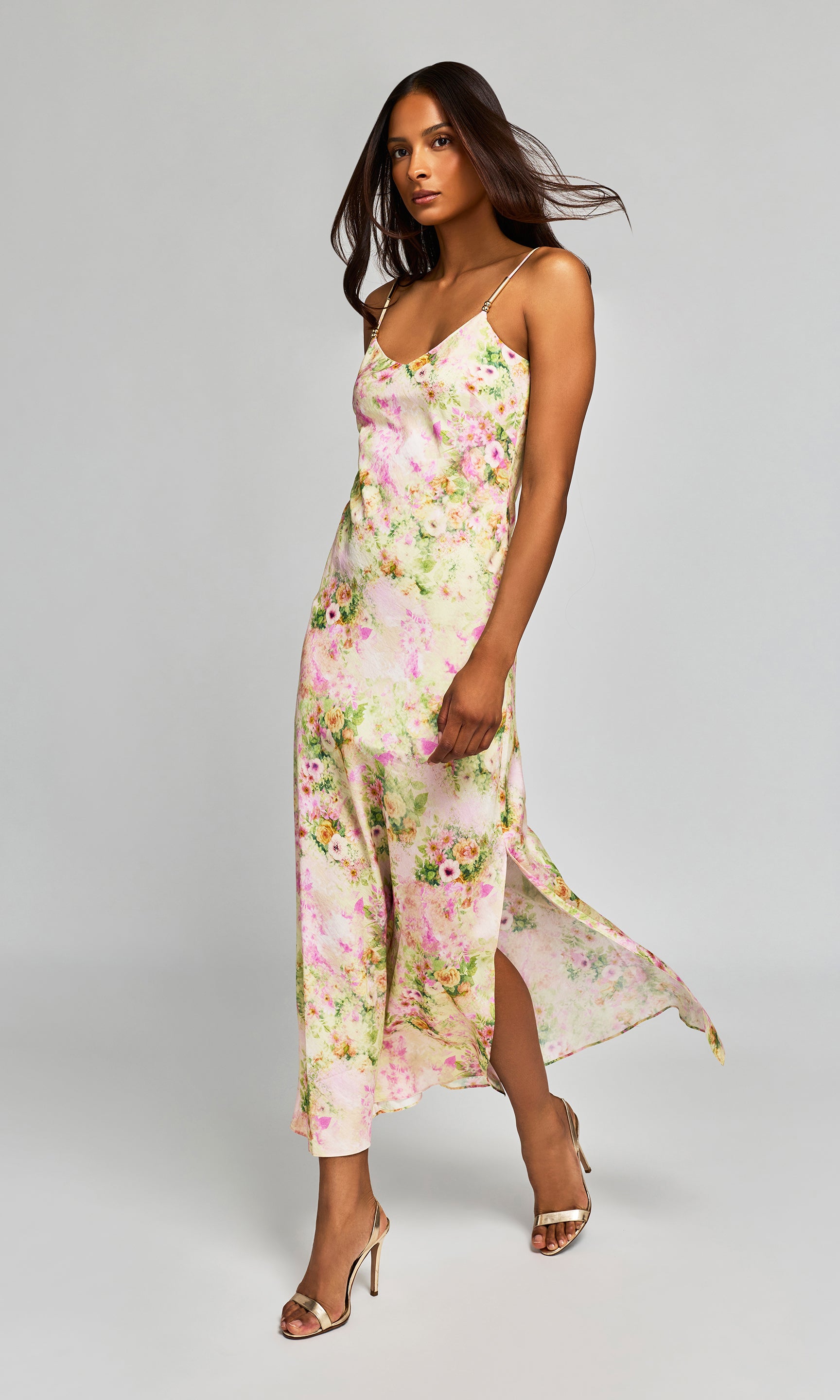Side view of woman wearing a floral dress with a side slit on a plain background.