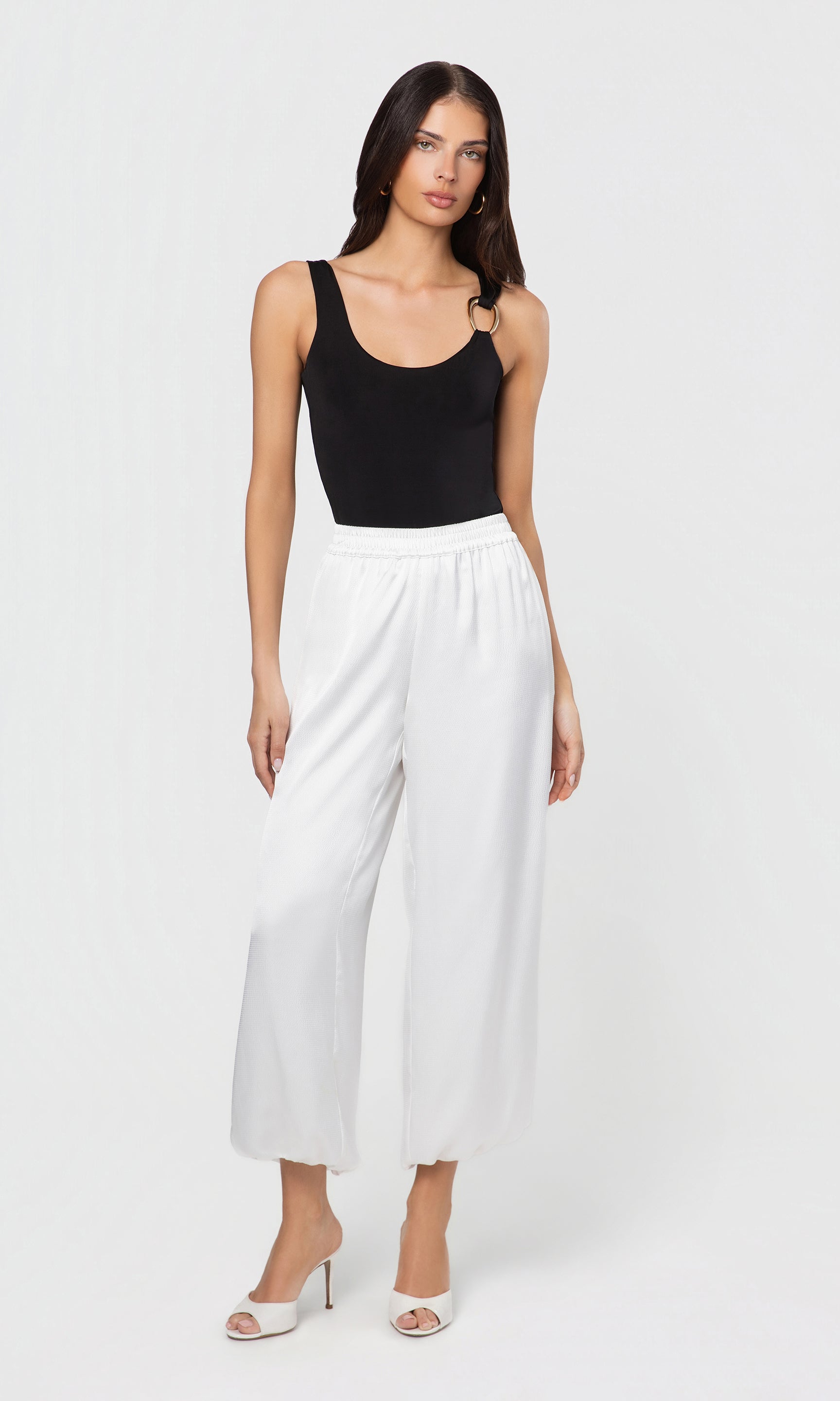 Woman wearing a black tank top and white wide-leg pants on a white background