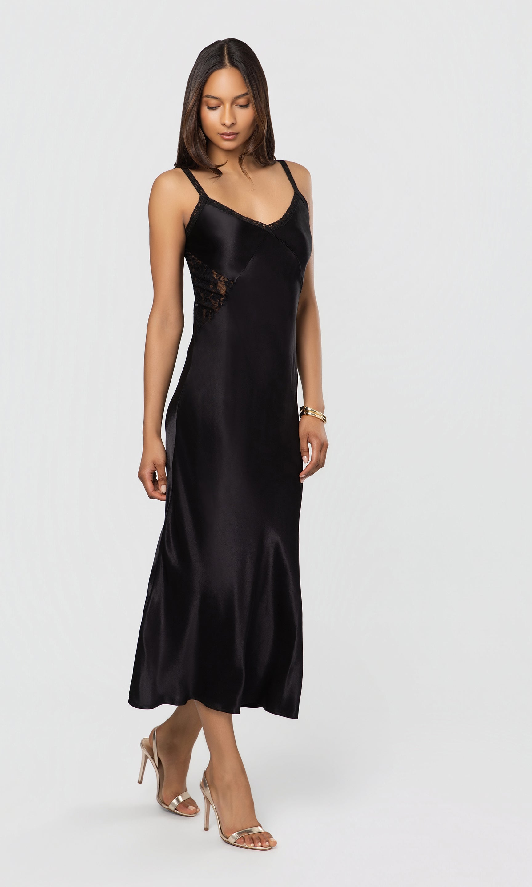 Side view of woman wearing a black slip dress on a white background