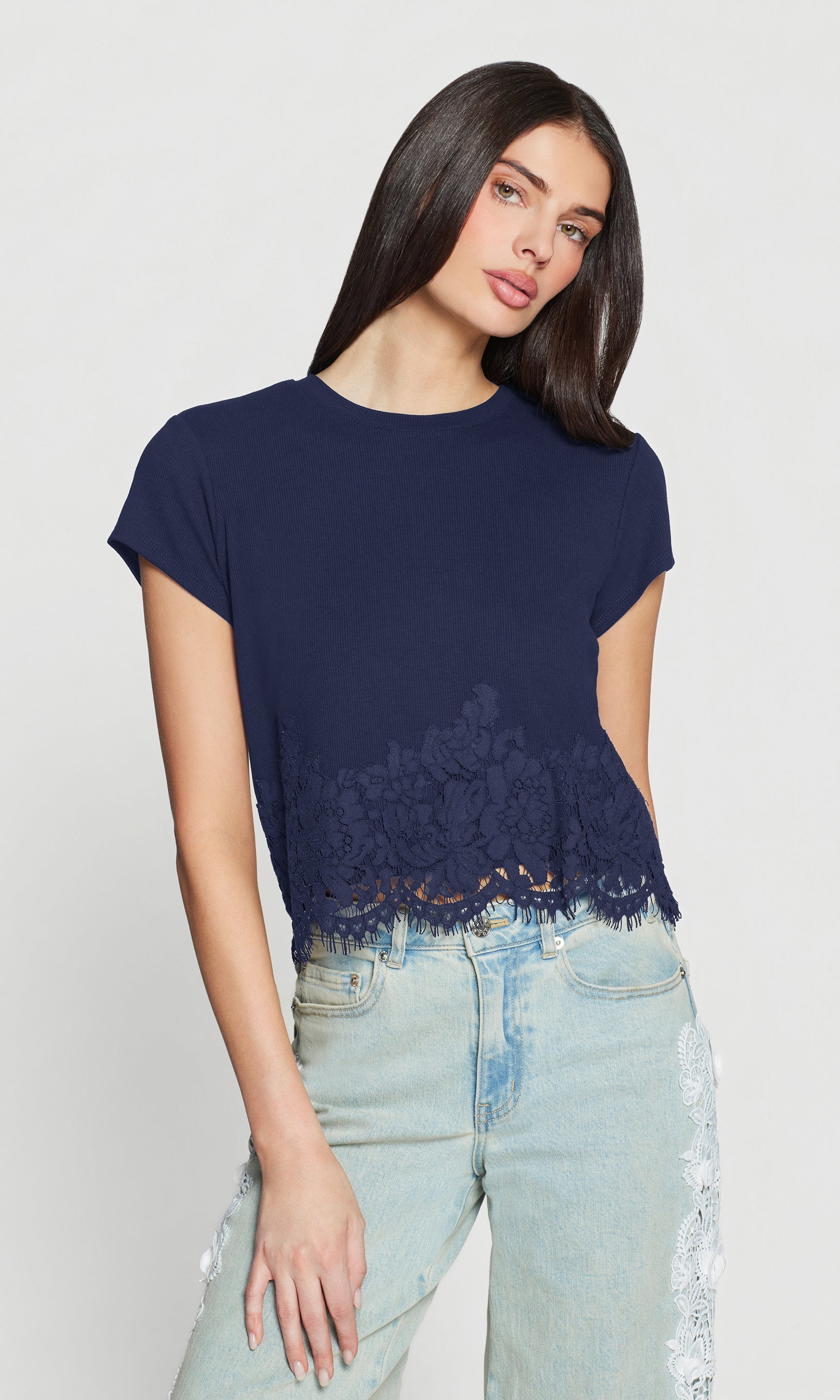 Woman wearing a navy blue t-shirt with lace trim and light blue jeans on a white background