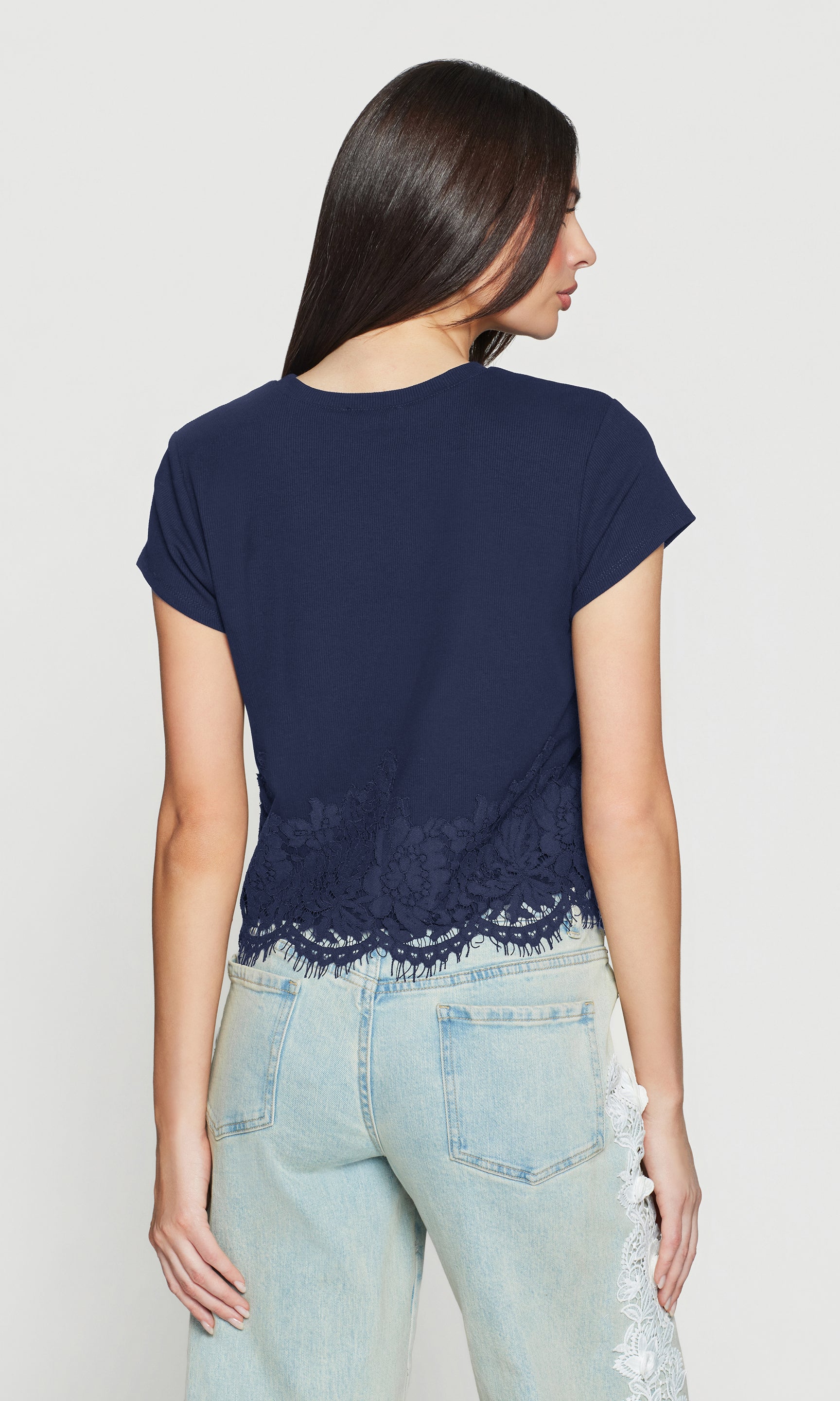 Back view of woman wearing a navy blue t-shirt with lace trim and light blue jeans on a white background