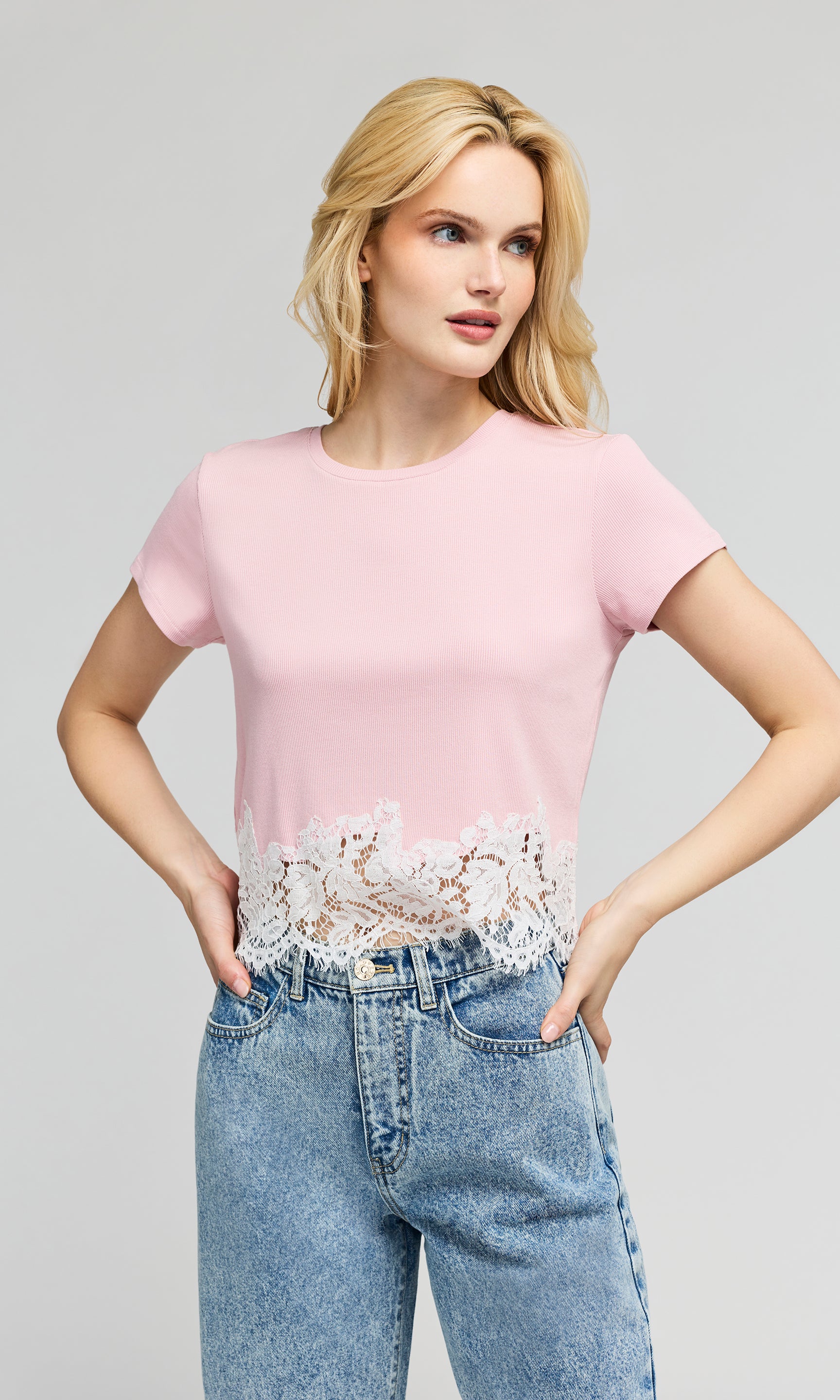 Woman wearing a pink top with lace details and blue jeans on a gray background