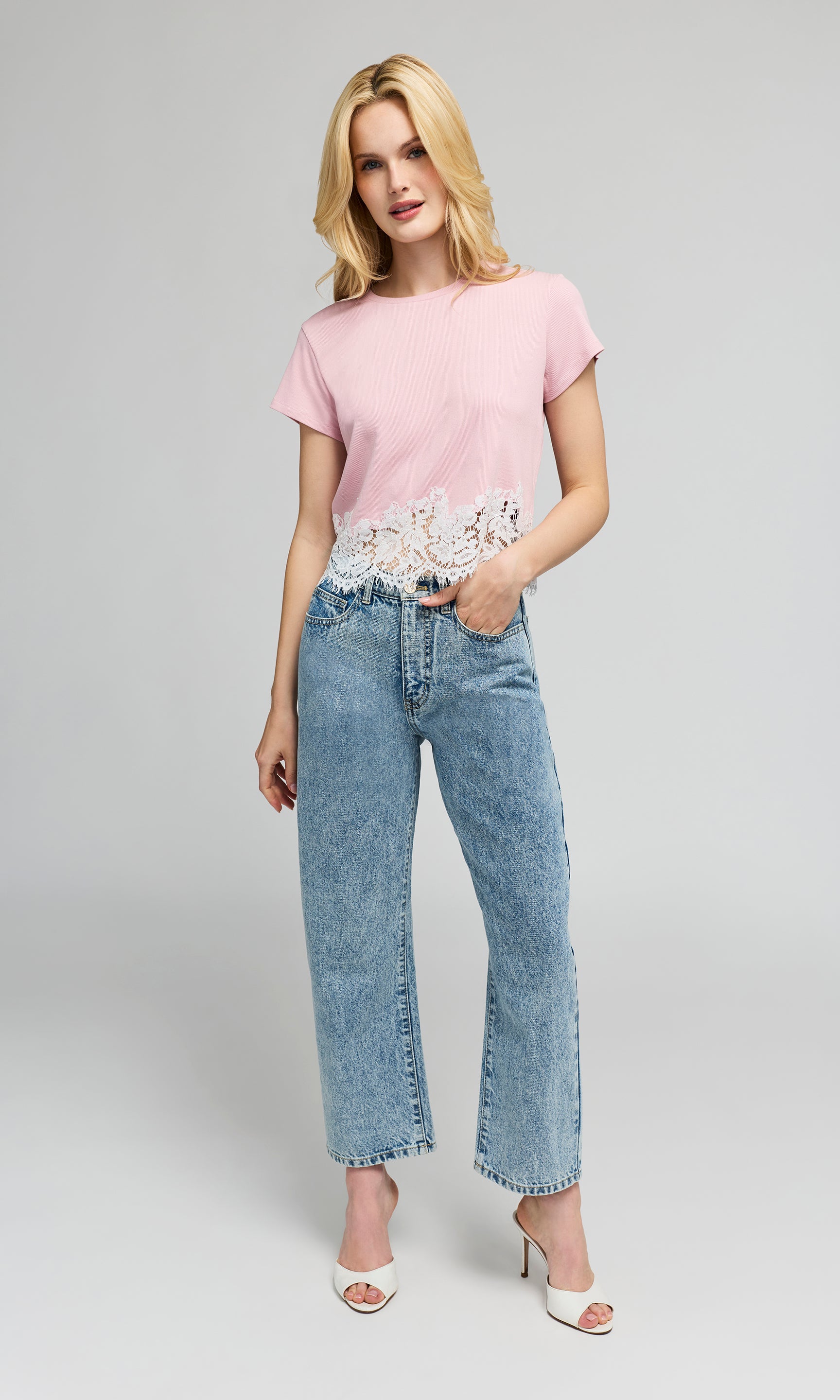 Woman wearing a pink top with lace detail and blue jeans on a gray background