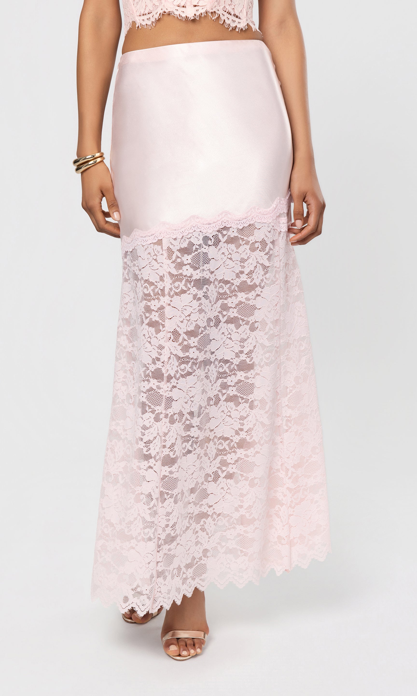 Person wearing a light pink lace skirt and top on a white background