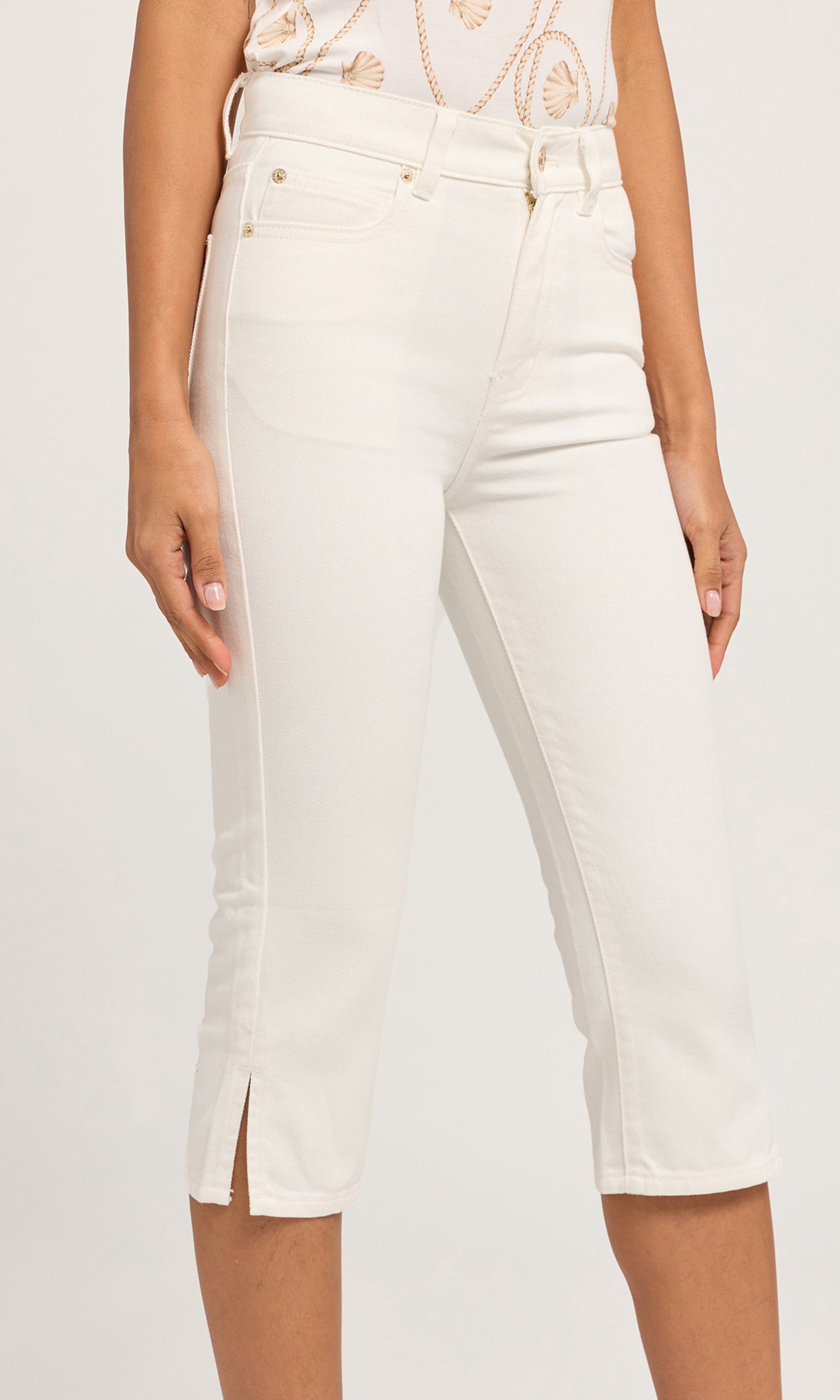 Close-up of cropped white denim jeans with side slits at the hem, paired with a patterned cream top.