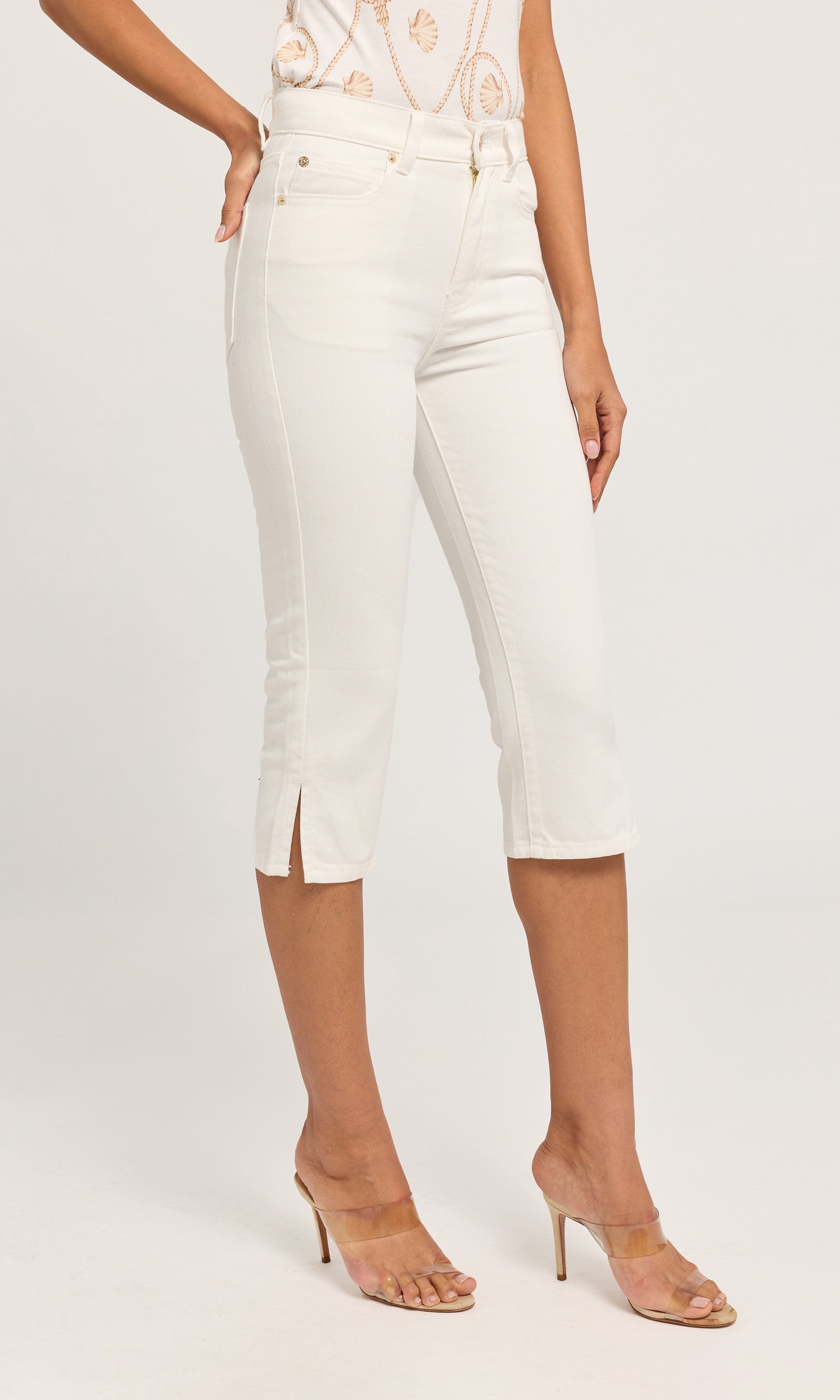 White cropped capri jeans with side slits, shown on a model wearing clear high-heeled sandals on a plain background.