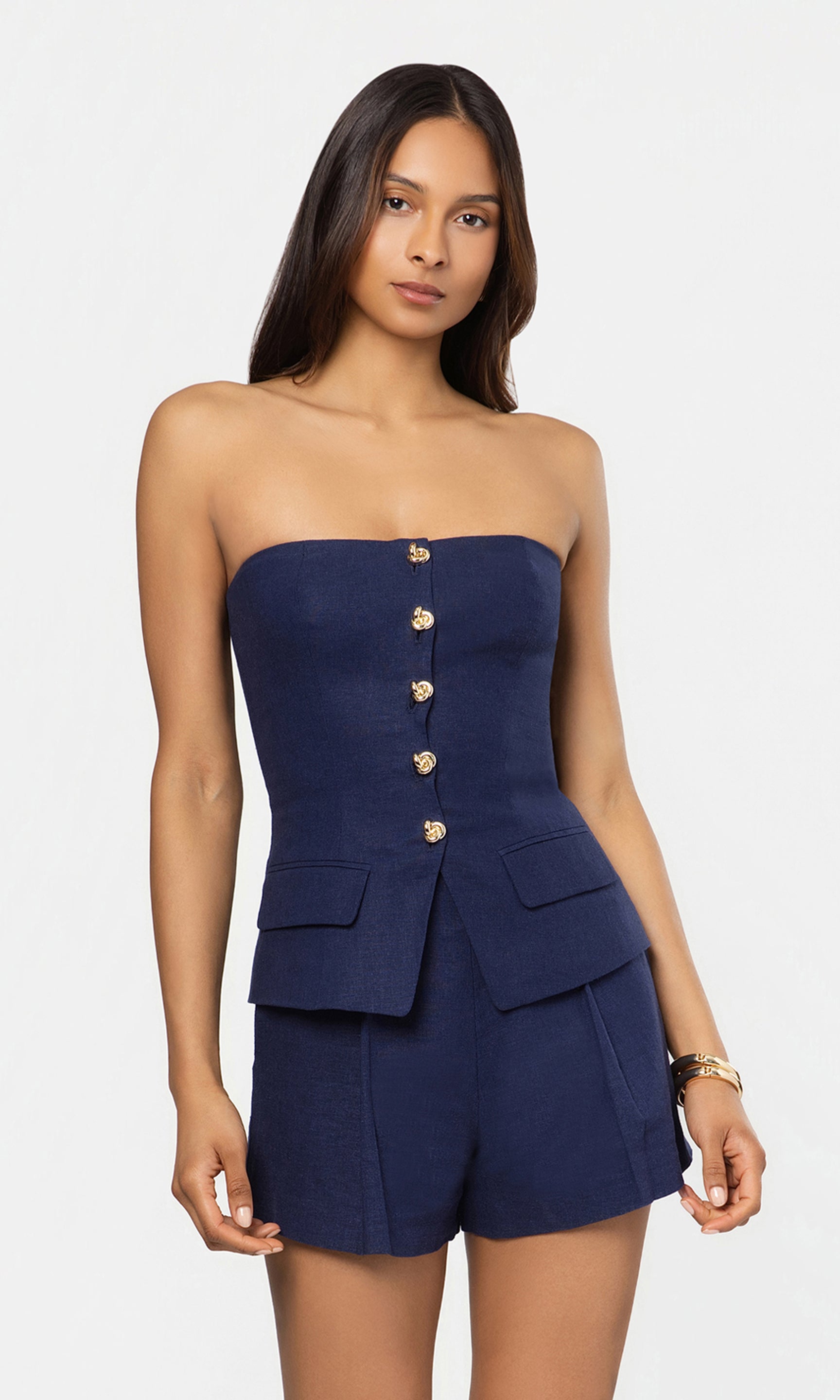 Woman wearing a strapless navy bustier and matching shorts with button details on a white background