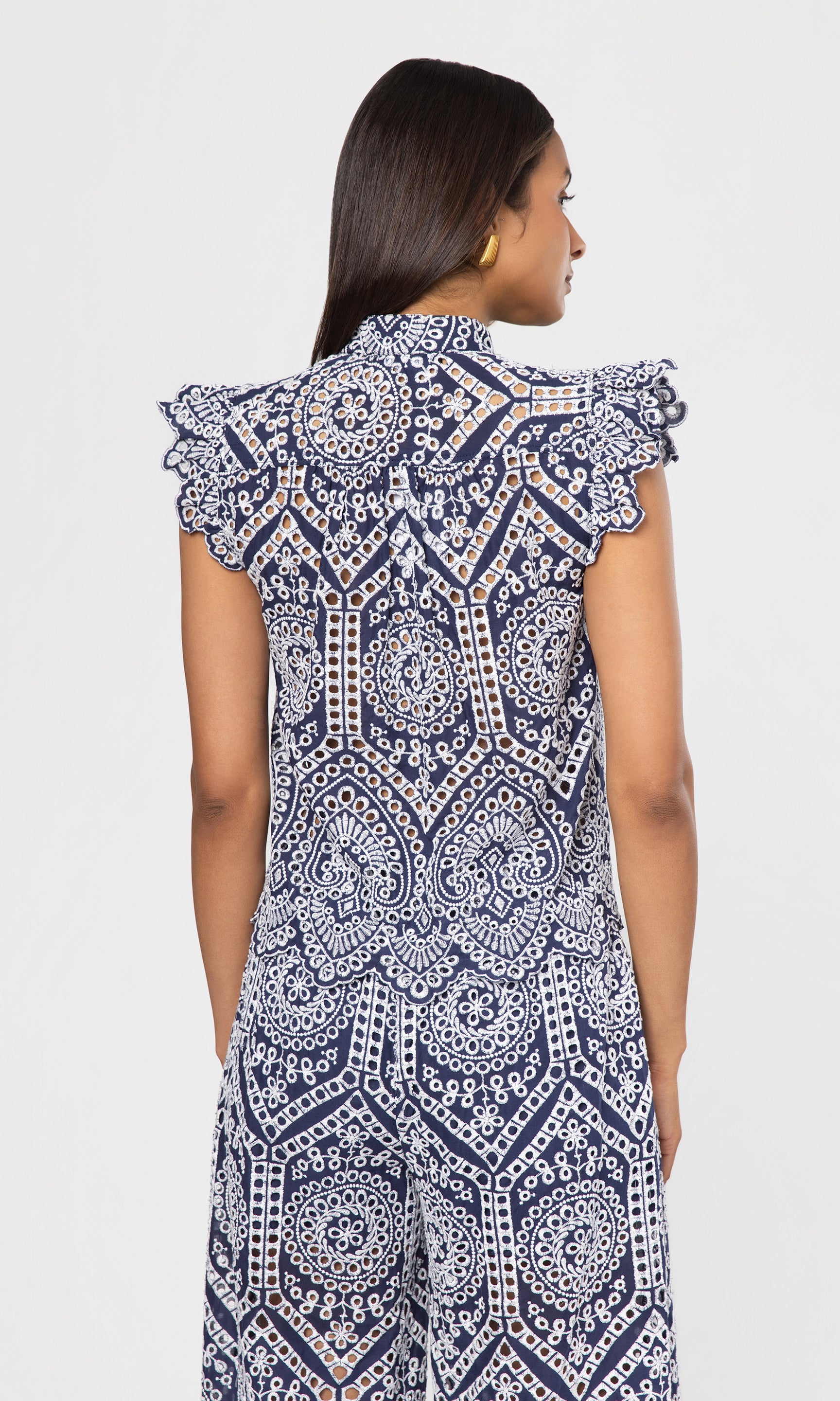 Back view of woman wearing a blue and white patterned top and pant on a plain background