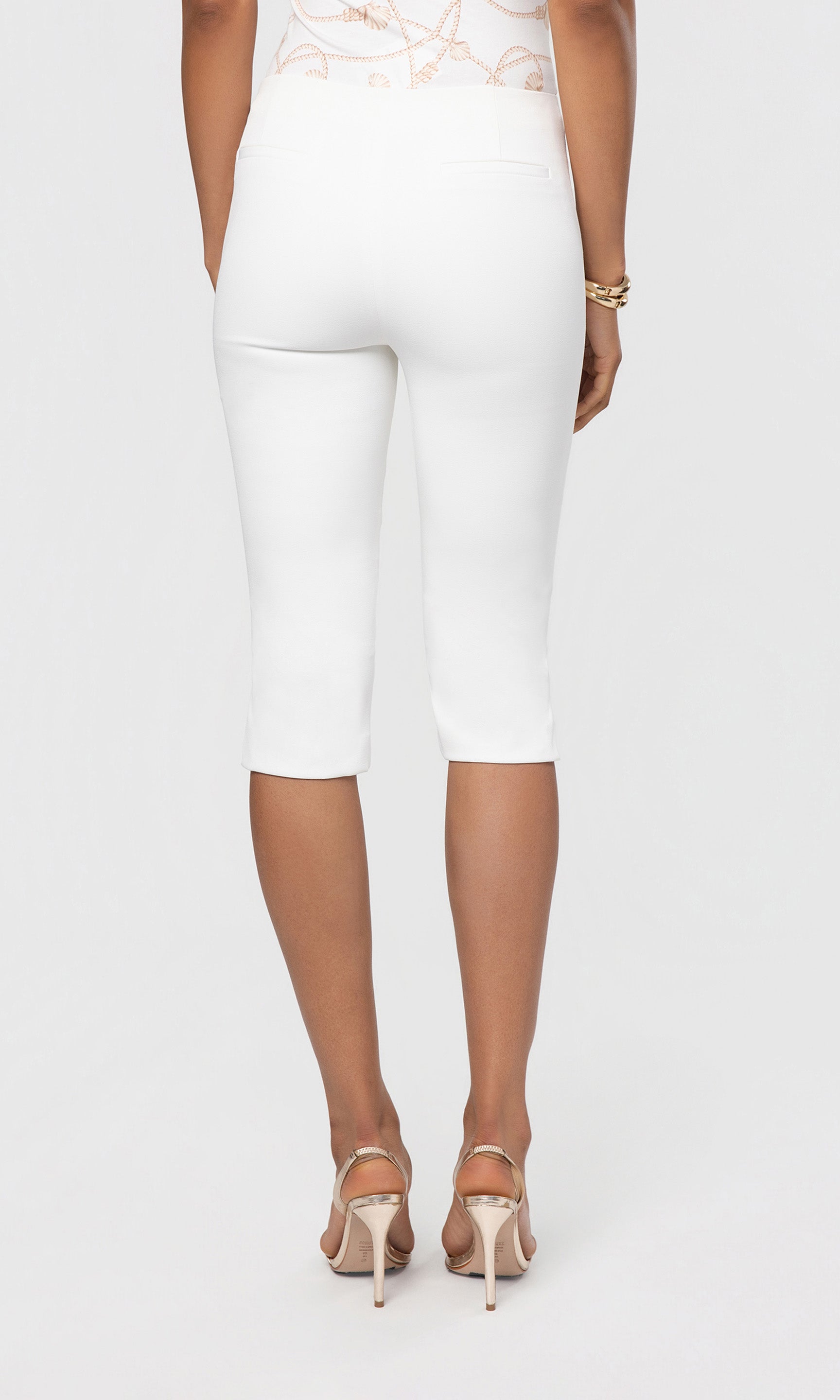 Back view of person wearing a white outfit with capri pants on a plain background