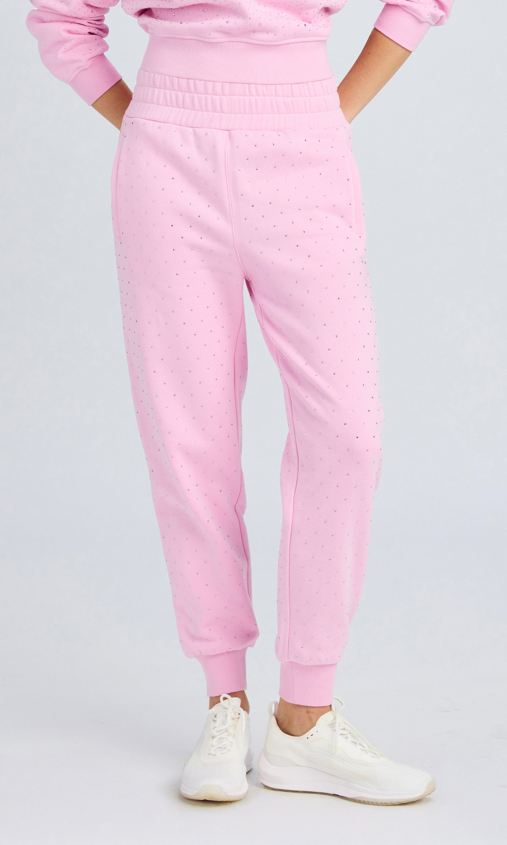 Model wearing poppy pink pants with crystal embellishments and a matching sweater on a plain background.