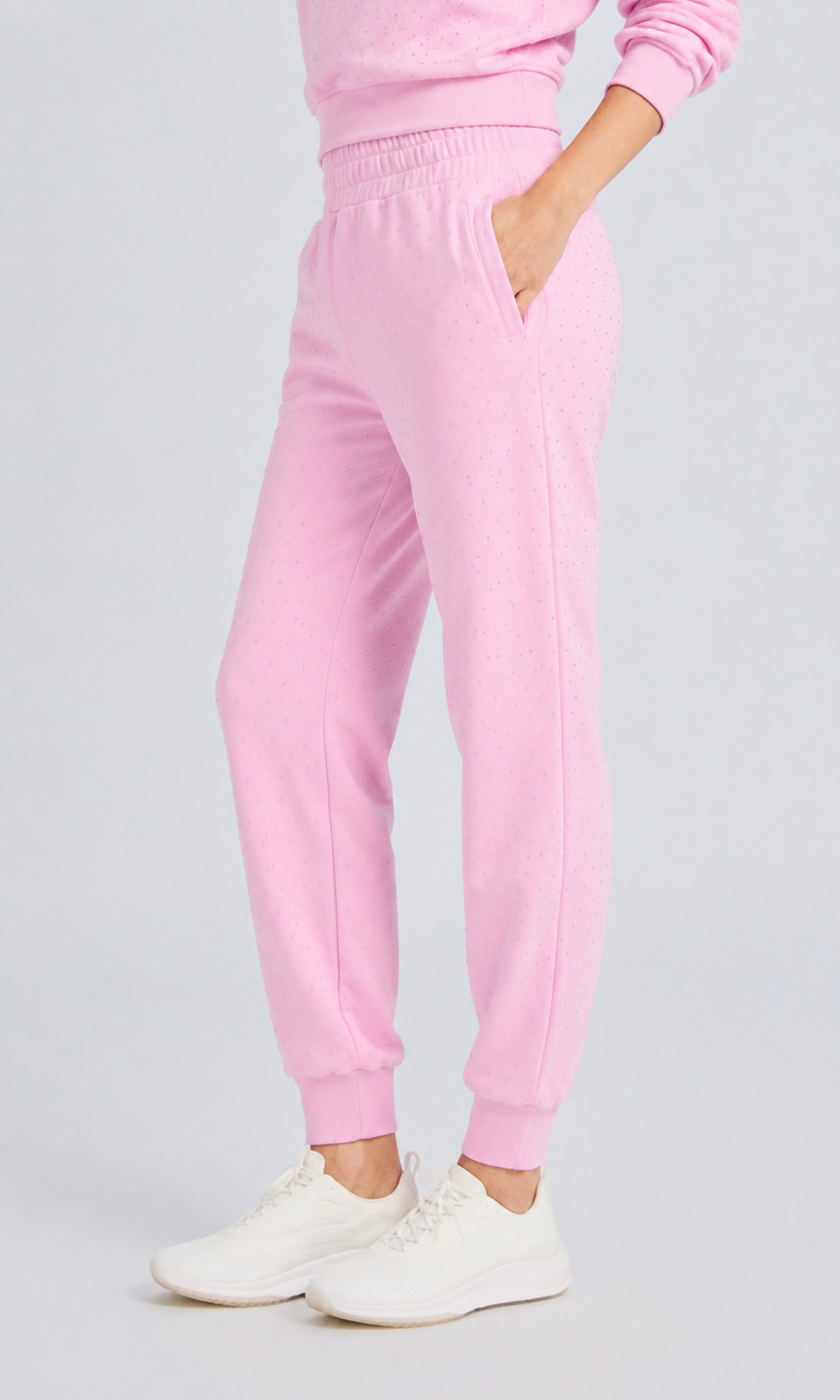 Side view of model wearing poppy pink pants with crystal embellishments and a matching sweater on a plain background.