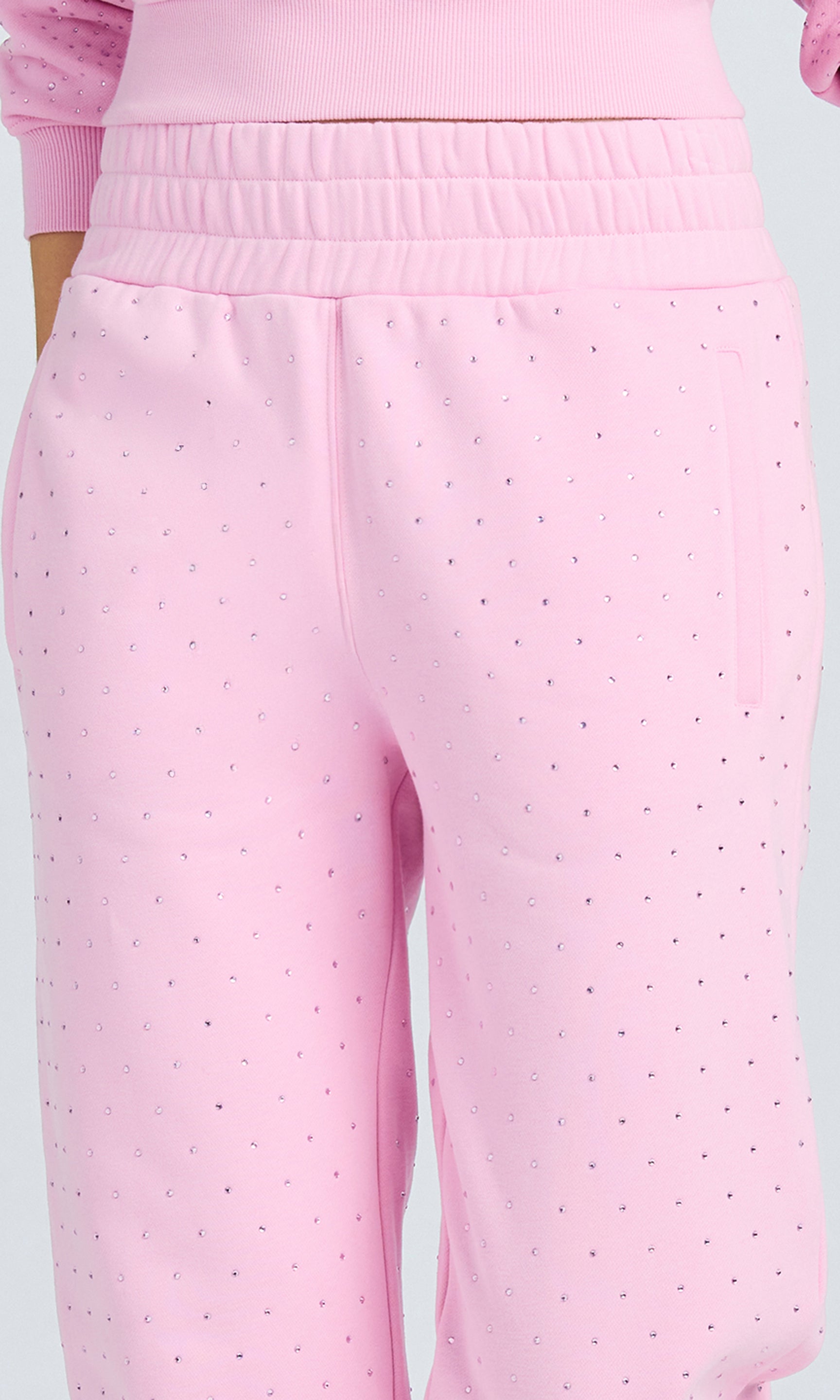 Close-up of model wearing poppy pink pants with crystal embellishments on a plain background.