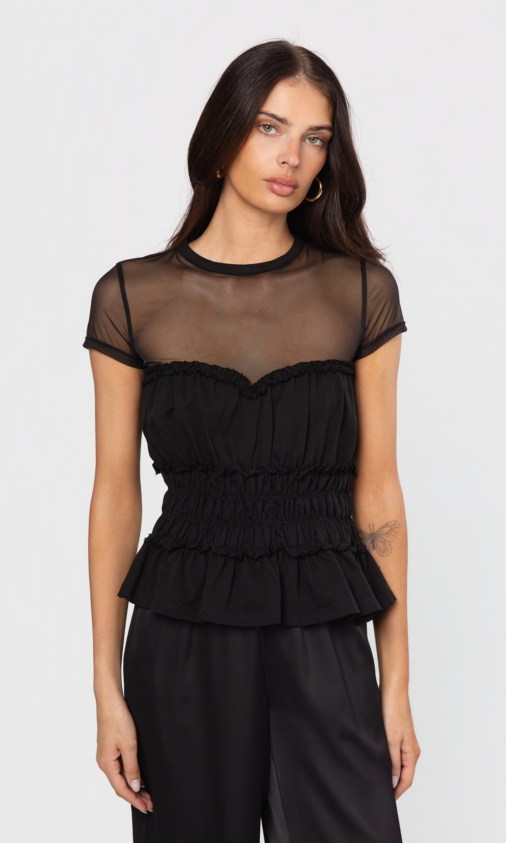 Woman wearing a black sheer top with ruffled details on a white background