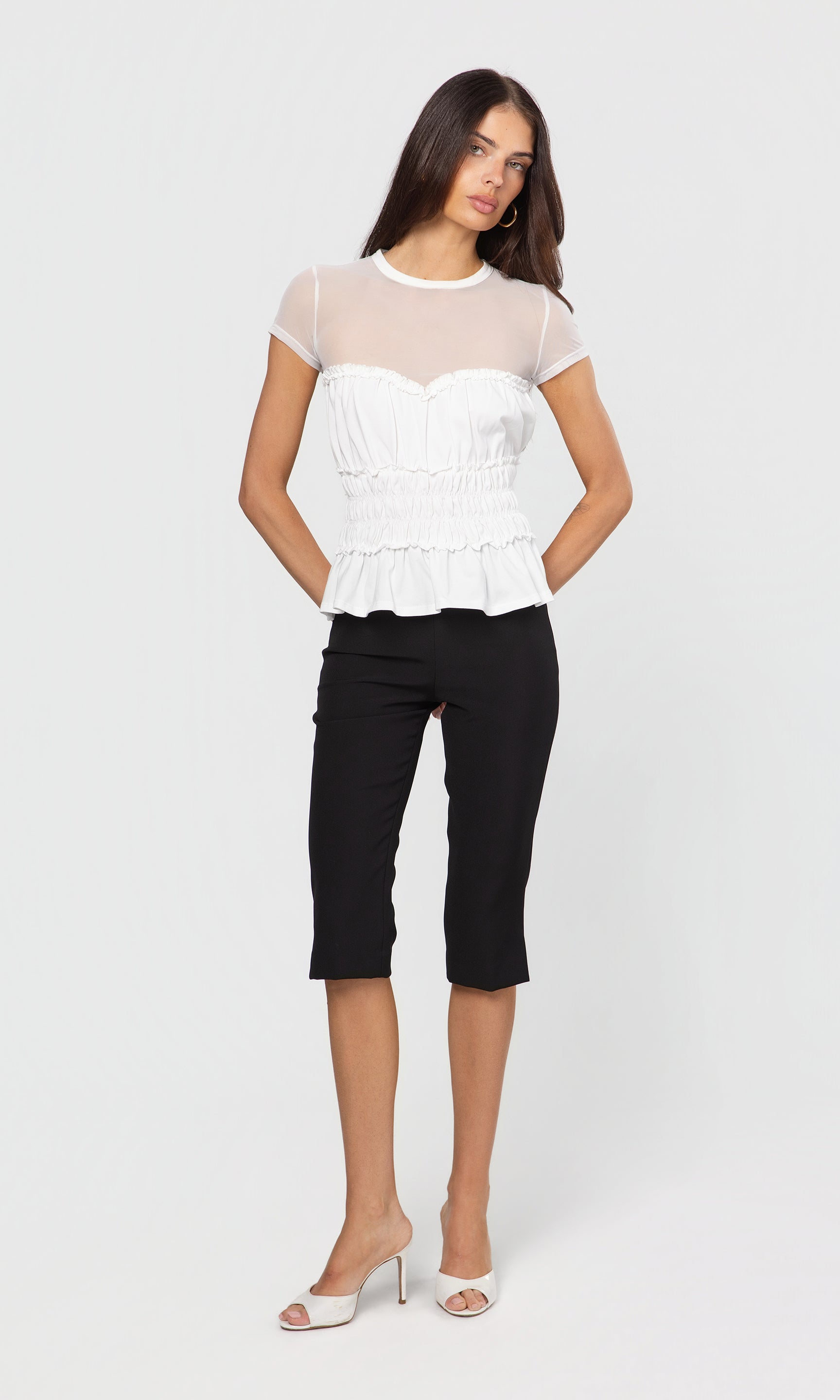 Woman wearing a white top with sheer sleeves and black capri pants on a white background