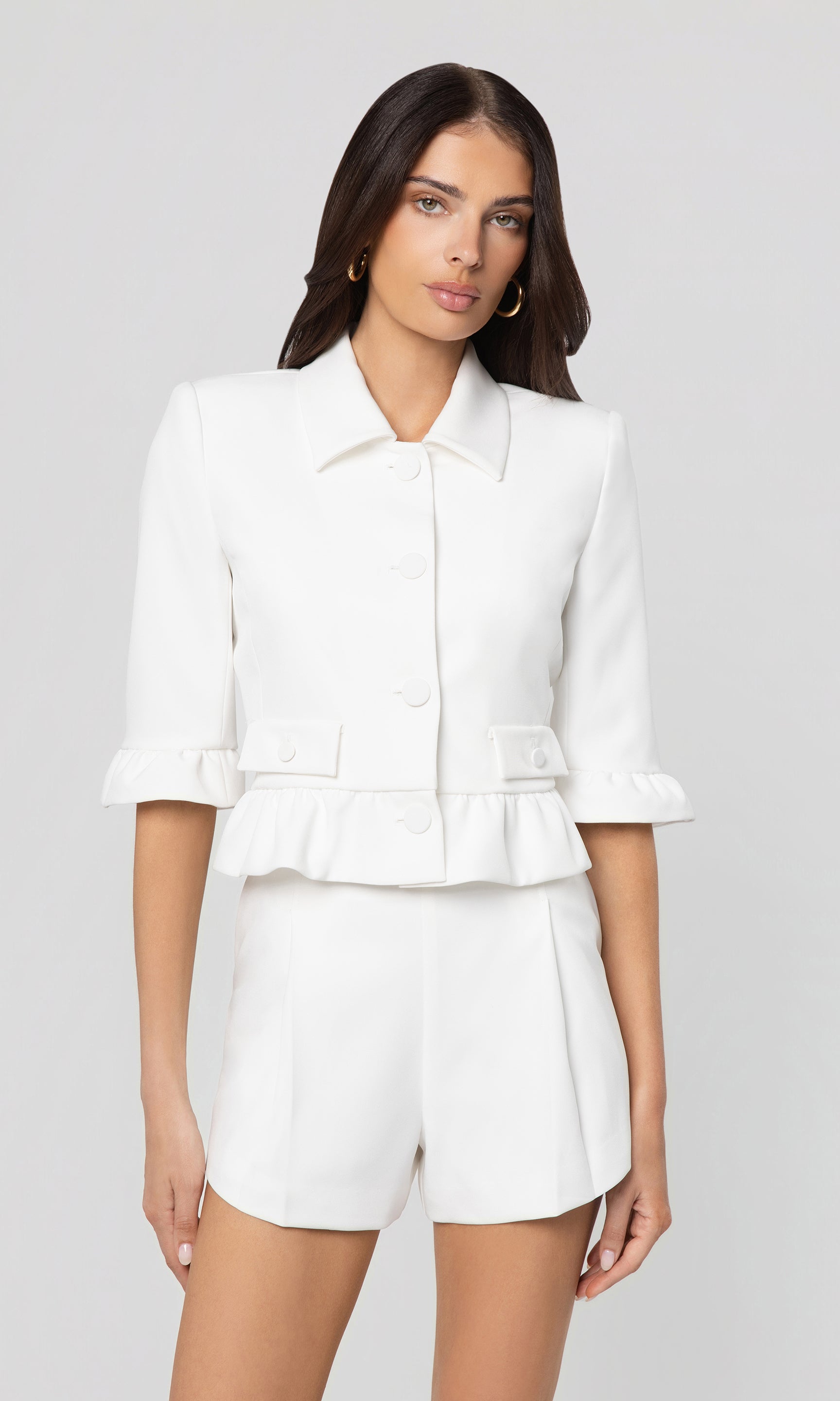 Woman wearing a white outfit with a jacket and shorts on a gray background