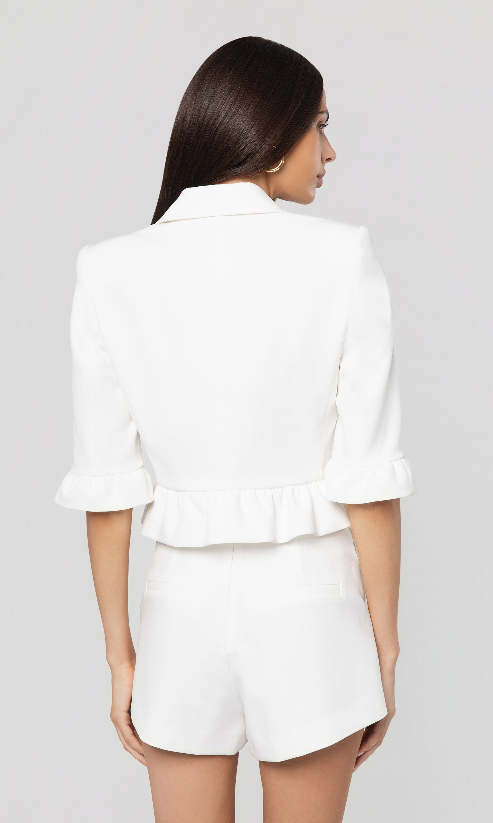 Back view of woman wearing a white blazer and shorts set on a gray background