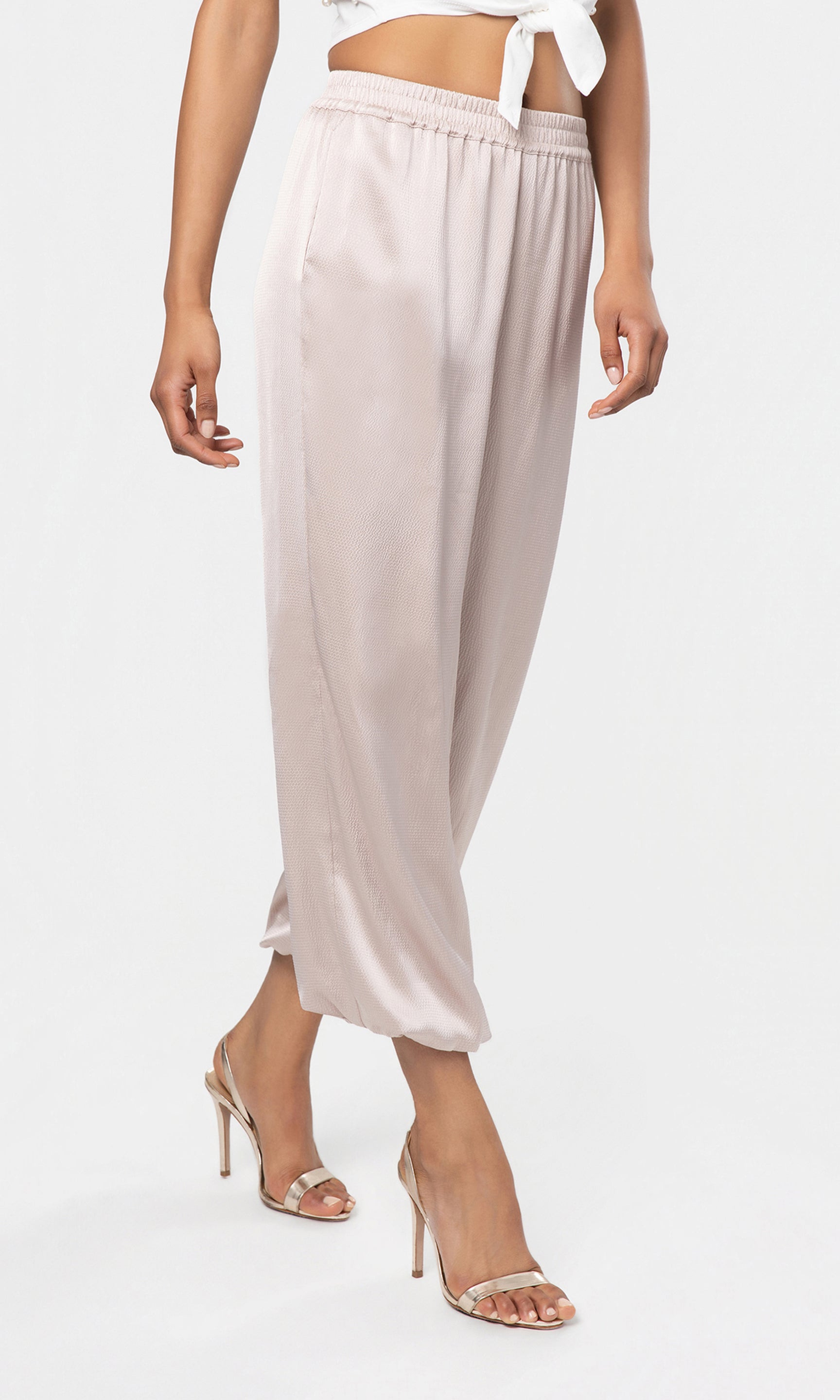 Side view of beige satin pants worn by a person on a white background