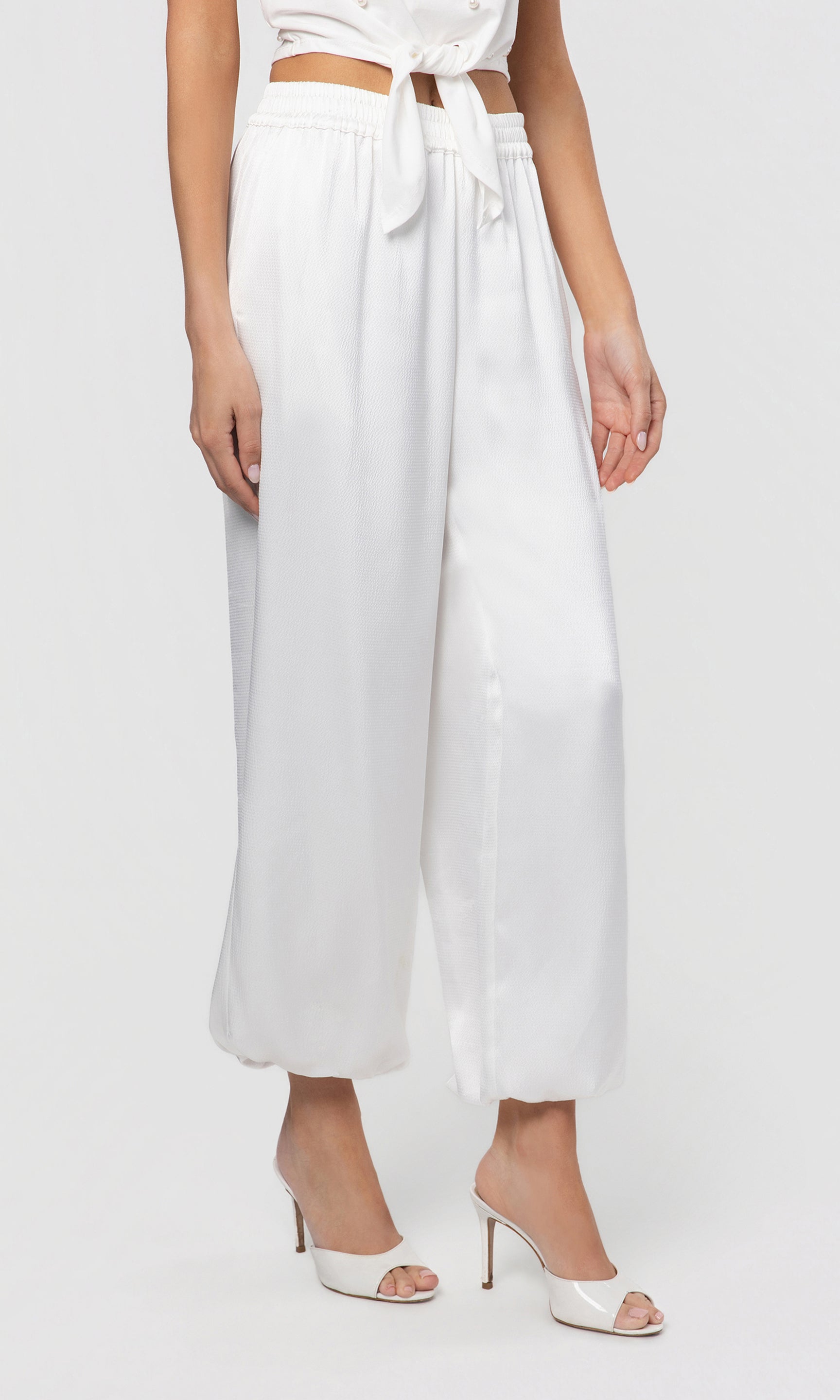 Side view of person wearing a white outfit with wide-leg pants on a plain background