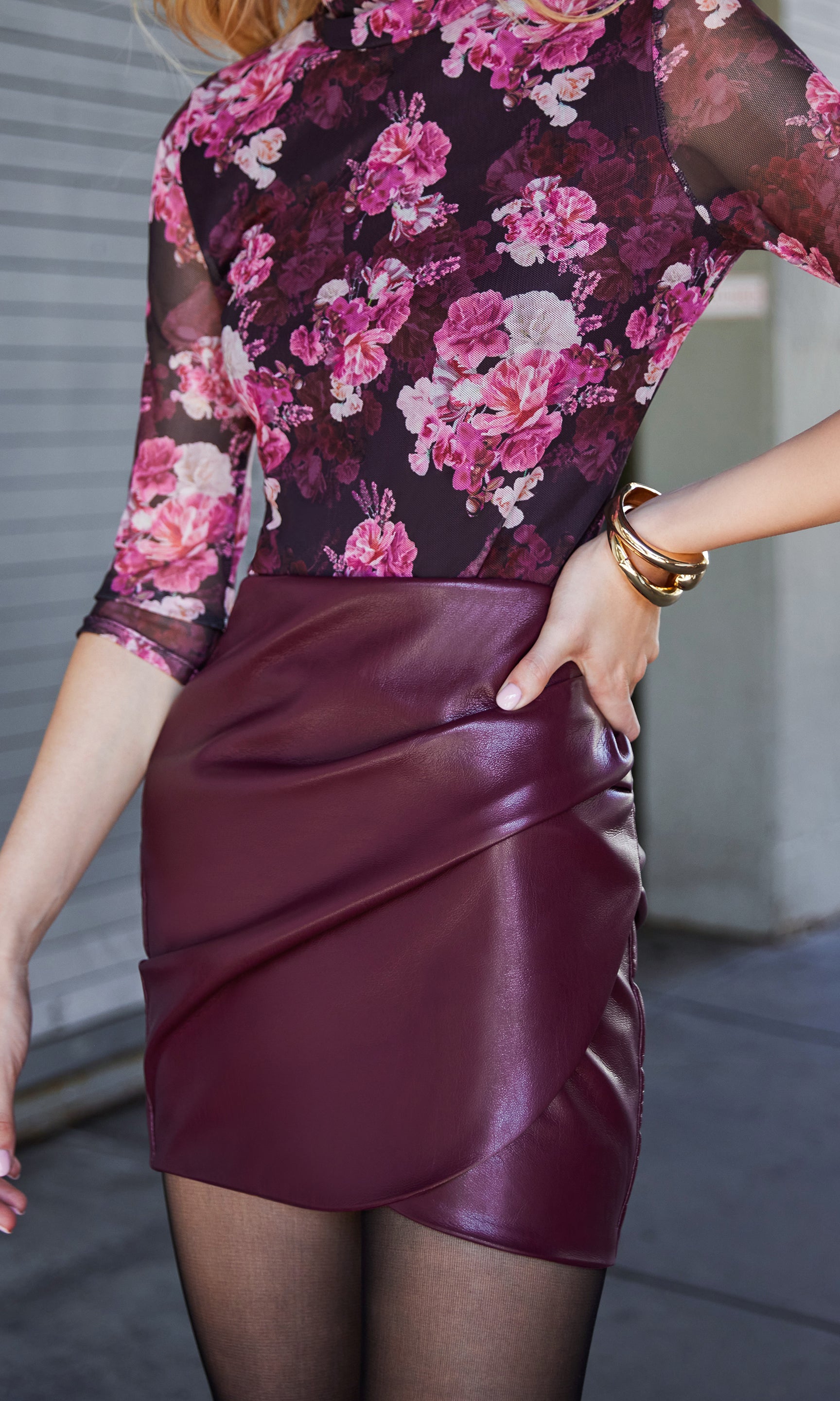 Person wearing a pink floral top and burgundy vegan leather skirt stands outside