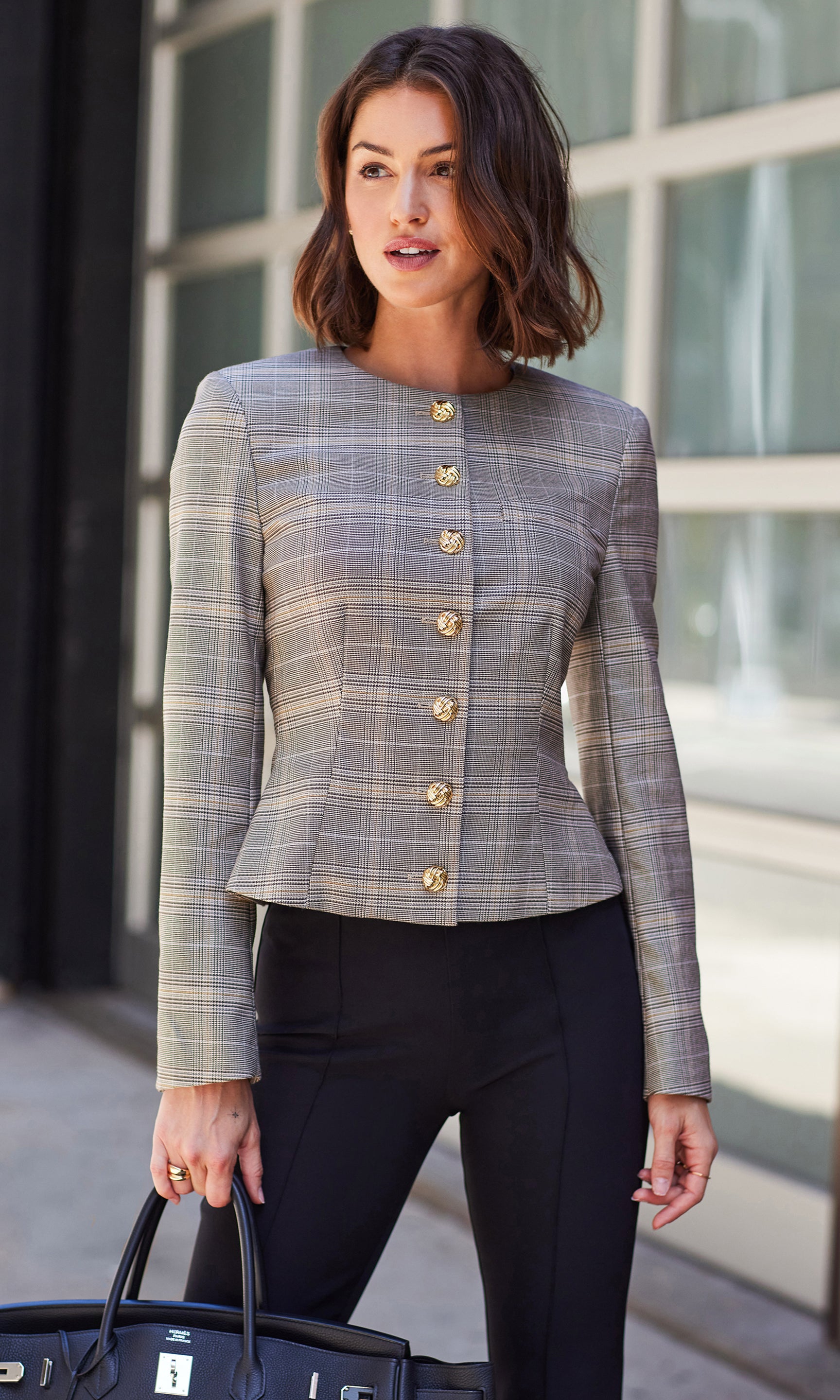 Woman wearing a plaid blazer with gold buttons outdoors.