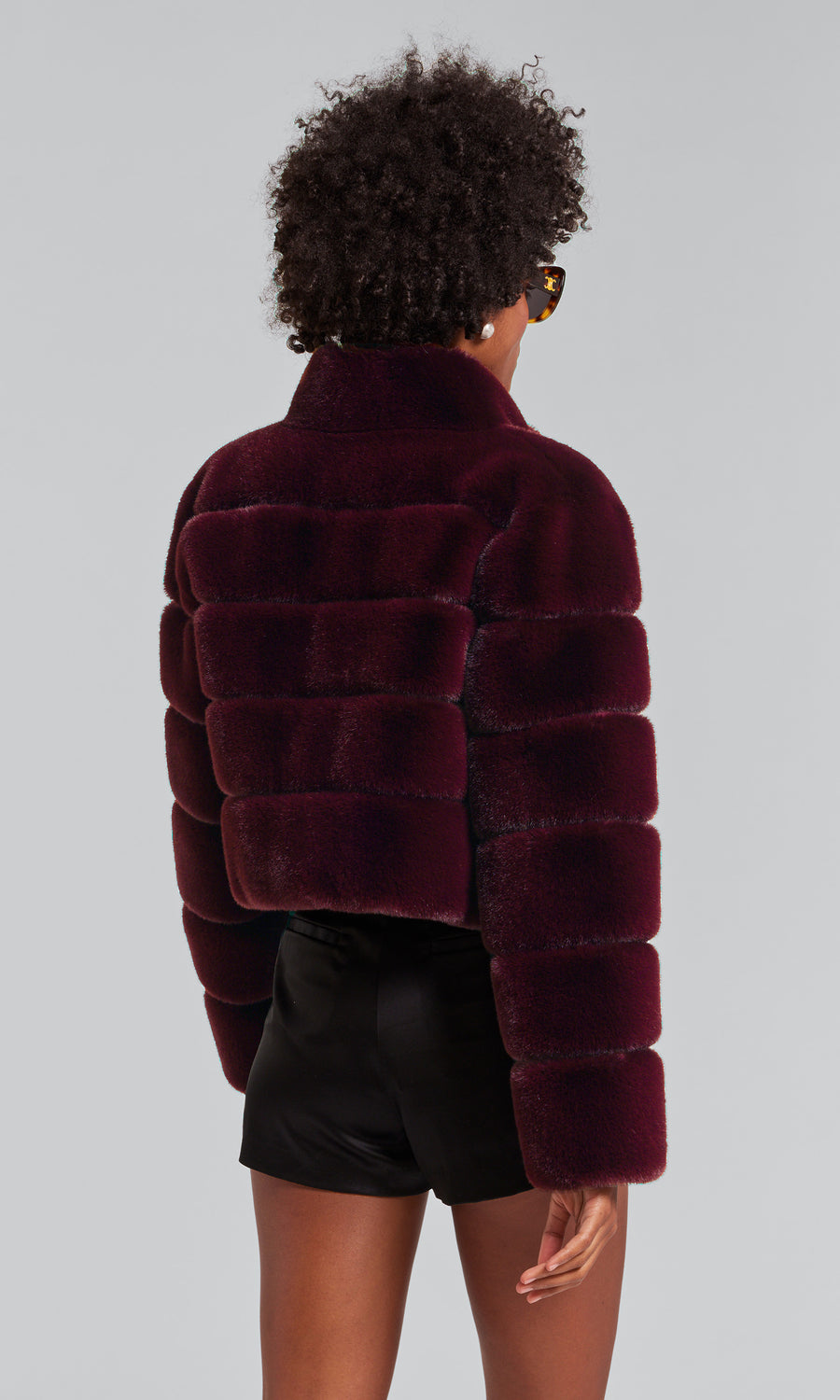 A woman models a malbec faux fur bomber coat, exuding sophistication and style in her fashionable attire.