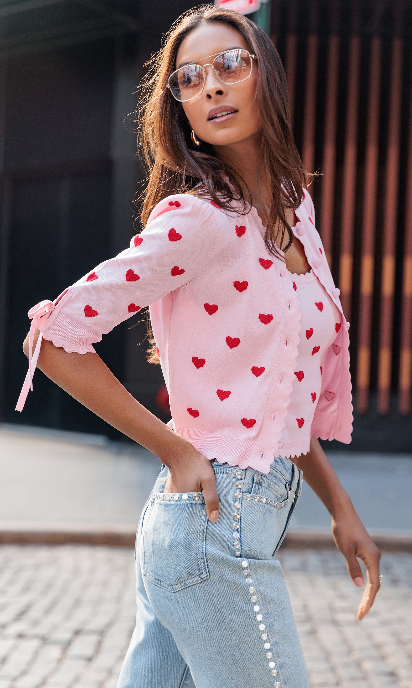 Woman wearing a pink blouse with red heart patterns and light blue jeans.