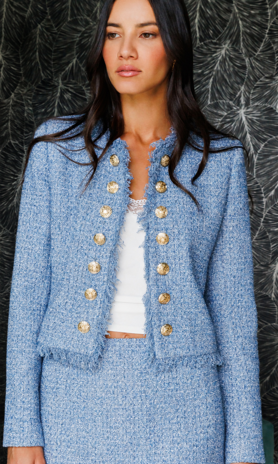 Woman wearing a blue tweed suit with gold buttons against a textured black and gray background