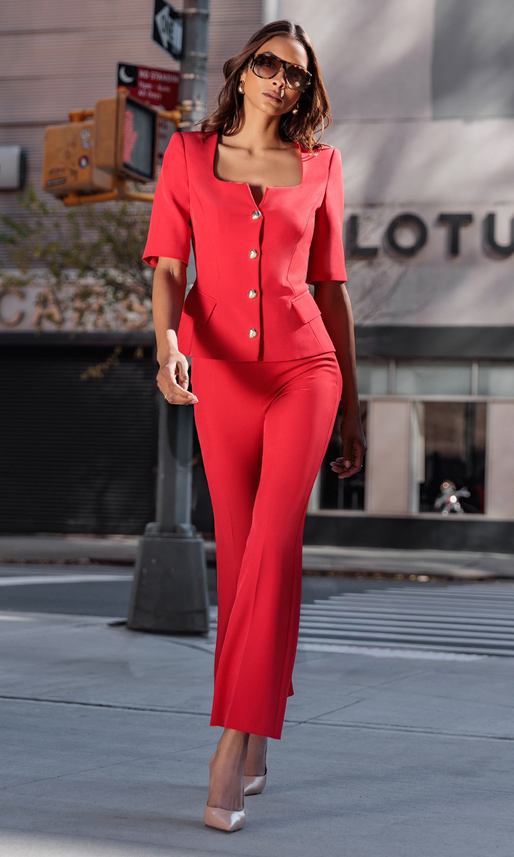 Woman in a red outfit walking on a city street with a Lotus building in the background.