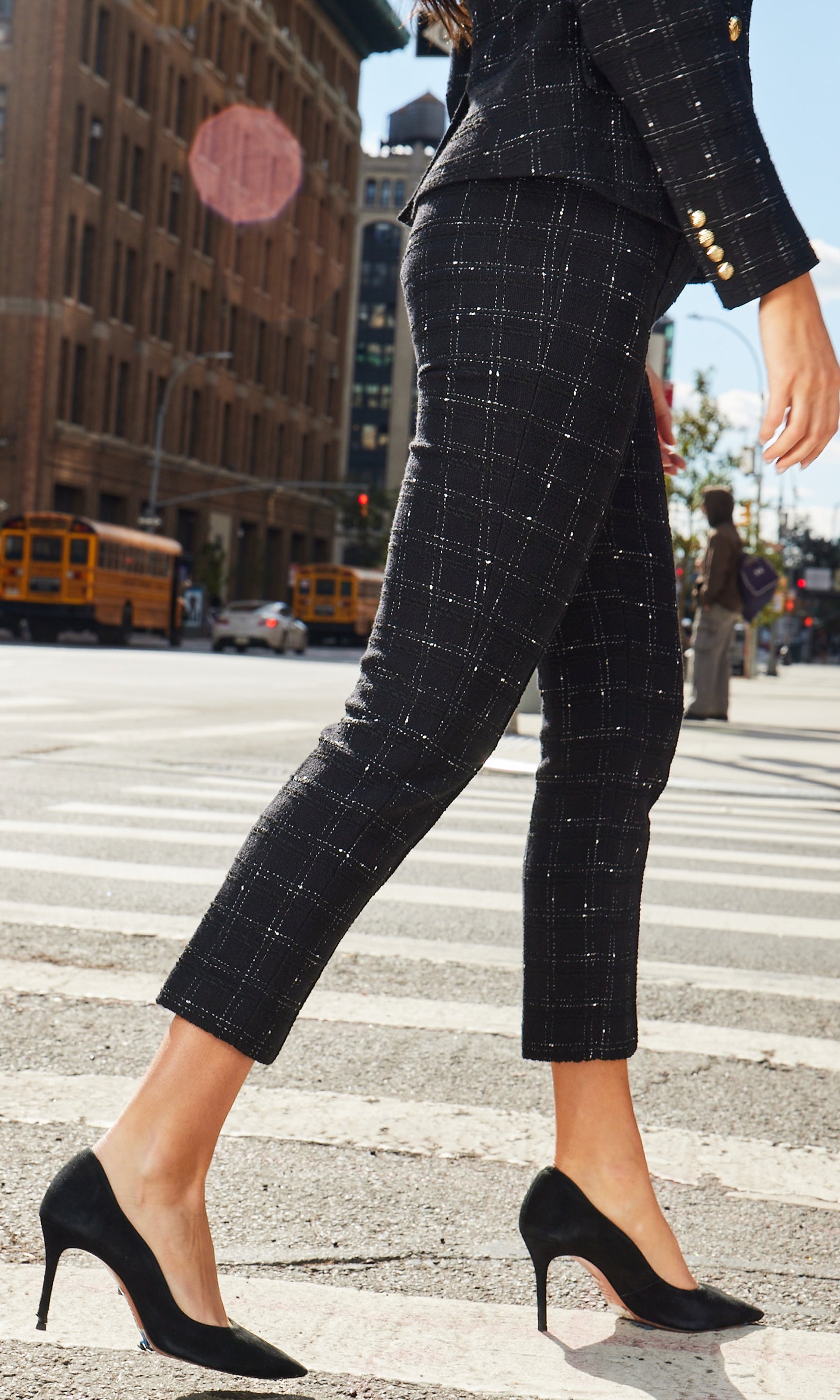 Side view of person wearing a black checkered suit crossing a street with urban background