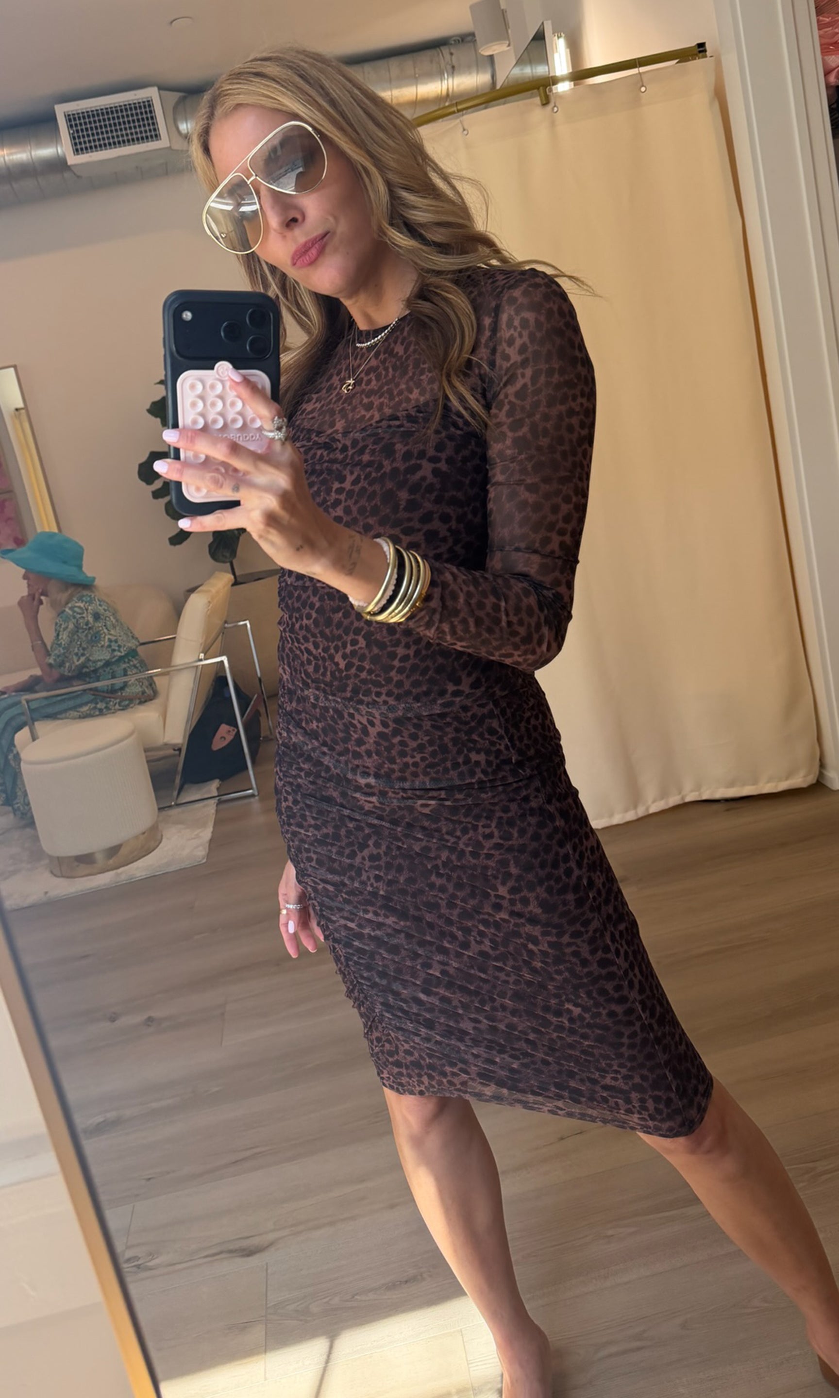 Our founder takes a mirror selfie in a fitting room wearing a sheer leopard-print top and skirt set. 