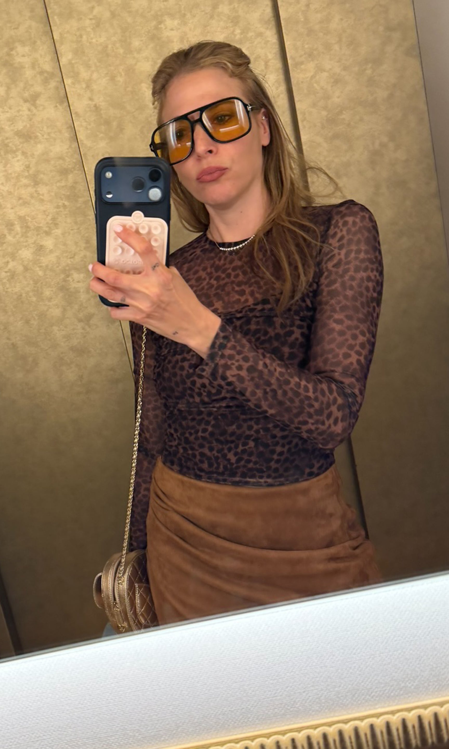 Founder Roni taking a mirror selfie wearing a sheer leopard-print long-sleeve top in brown and black, paired with a brown skirt.