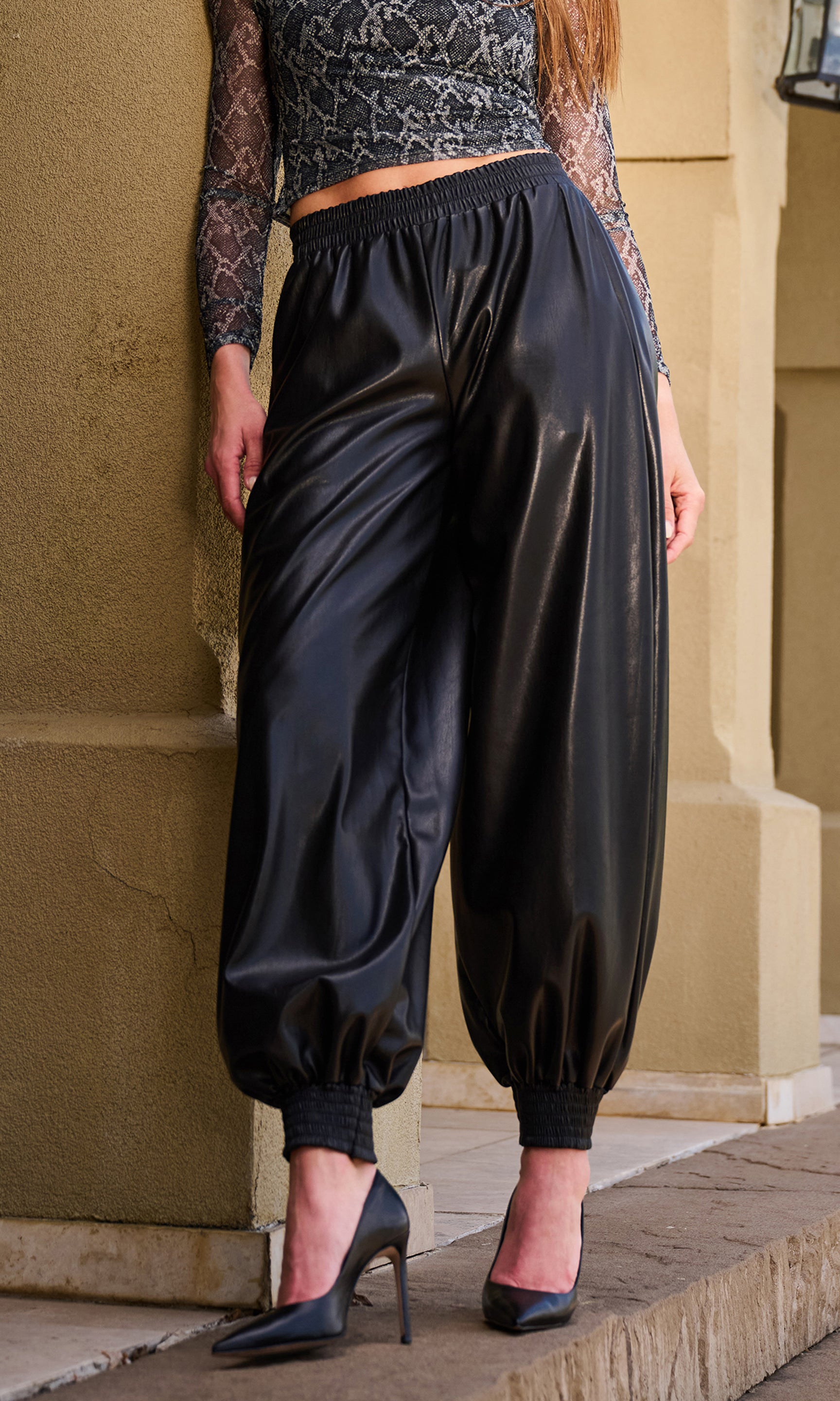 A person wearing shiny black harem-style pants with elastic cuffs, paired with a snake-print crop top.