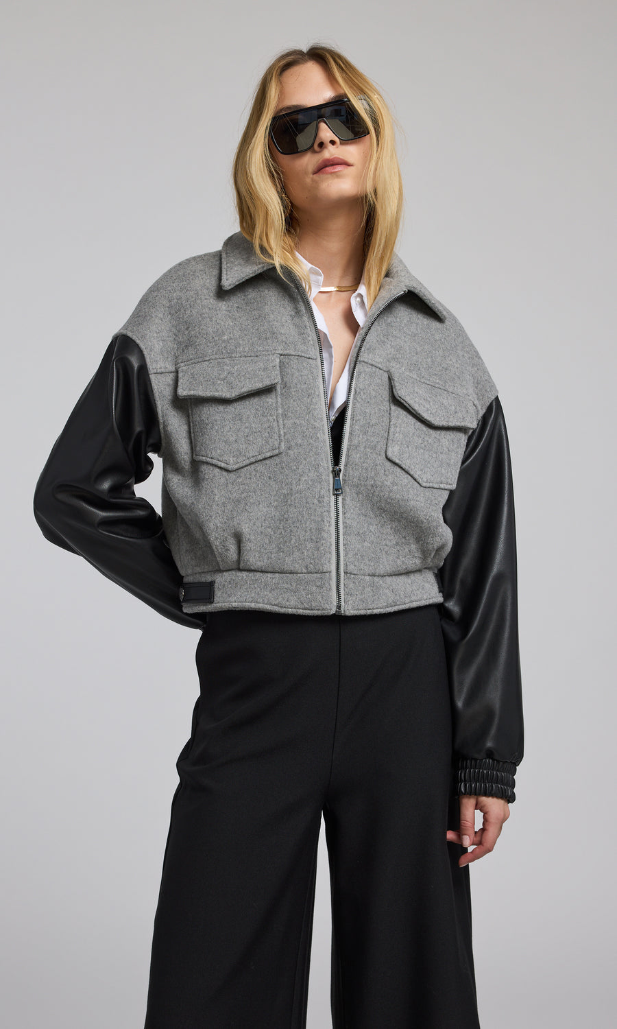 The model presents a grey bomber jacket made of wool, complemented by sleek black vegan leather sleeves.