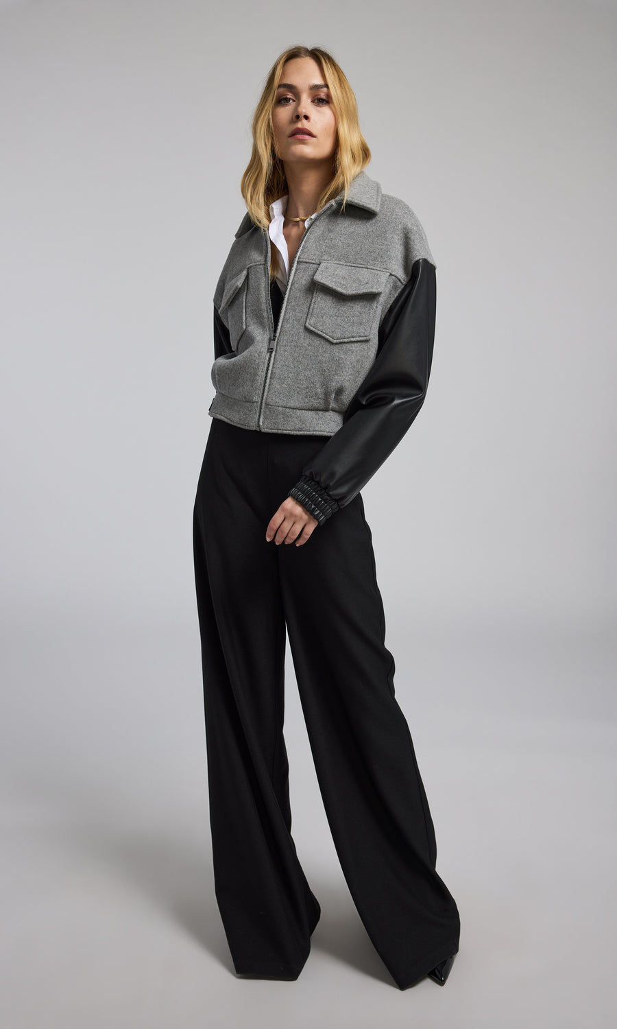 The model presents a grey bomber jacket made of wool, complemented by sleek black vegan leather sleeves.