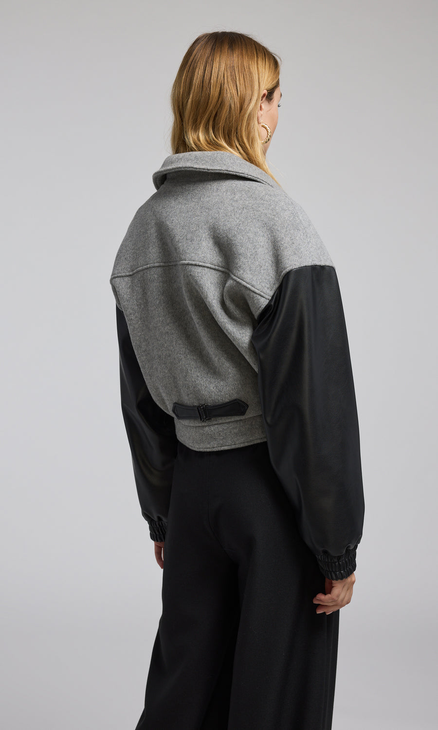 The model presents a grey bomber jacket made of wool, complemented by sleek black vegan leather sleeves.