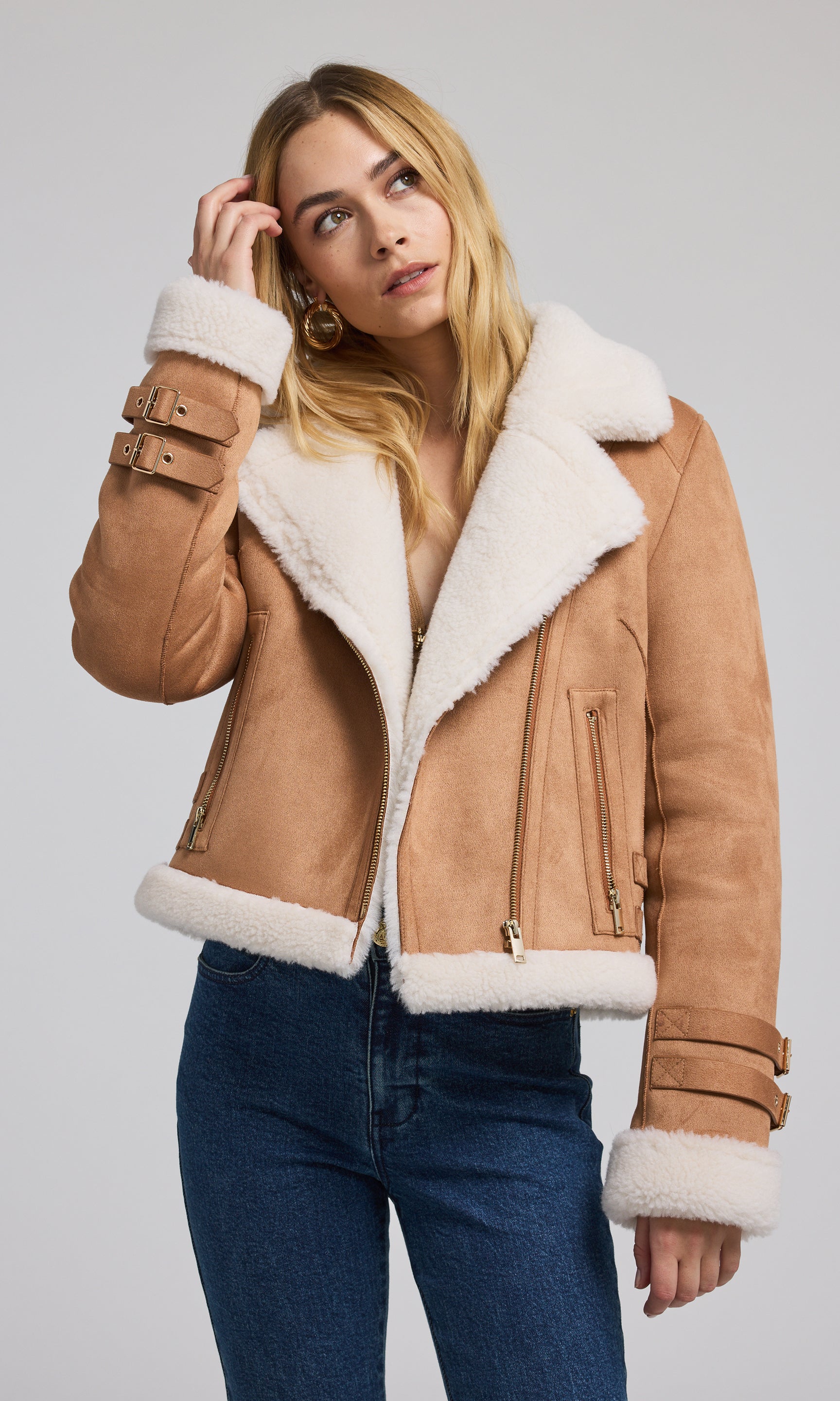 The image features a tan vegan suede shearling Moto jacket, highlighting its sleek and fashionable appearance.