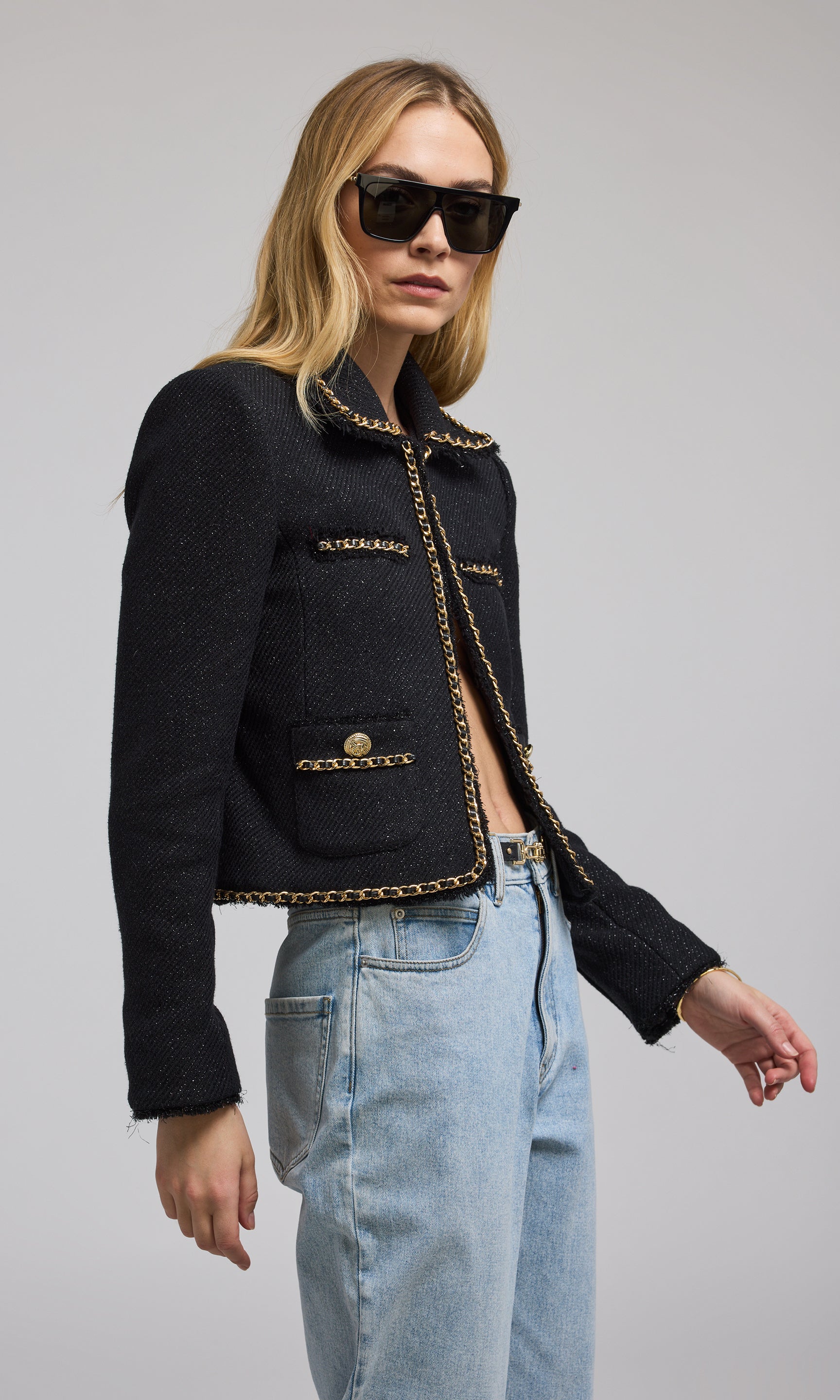 A woman models a stylish black tweed jacket adorned with elegant gold buttons and gold chain, showcasing a sophisticated look.
