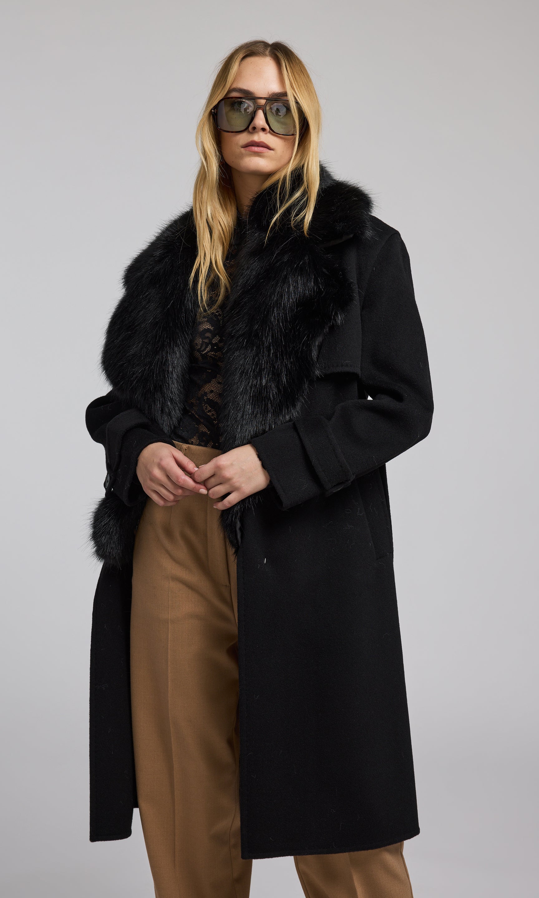 A model is seen wearing a sleek black coat with a fur collar, emphasizing a refined and fashionable outerwear choice.