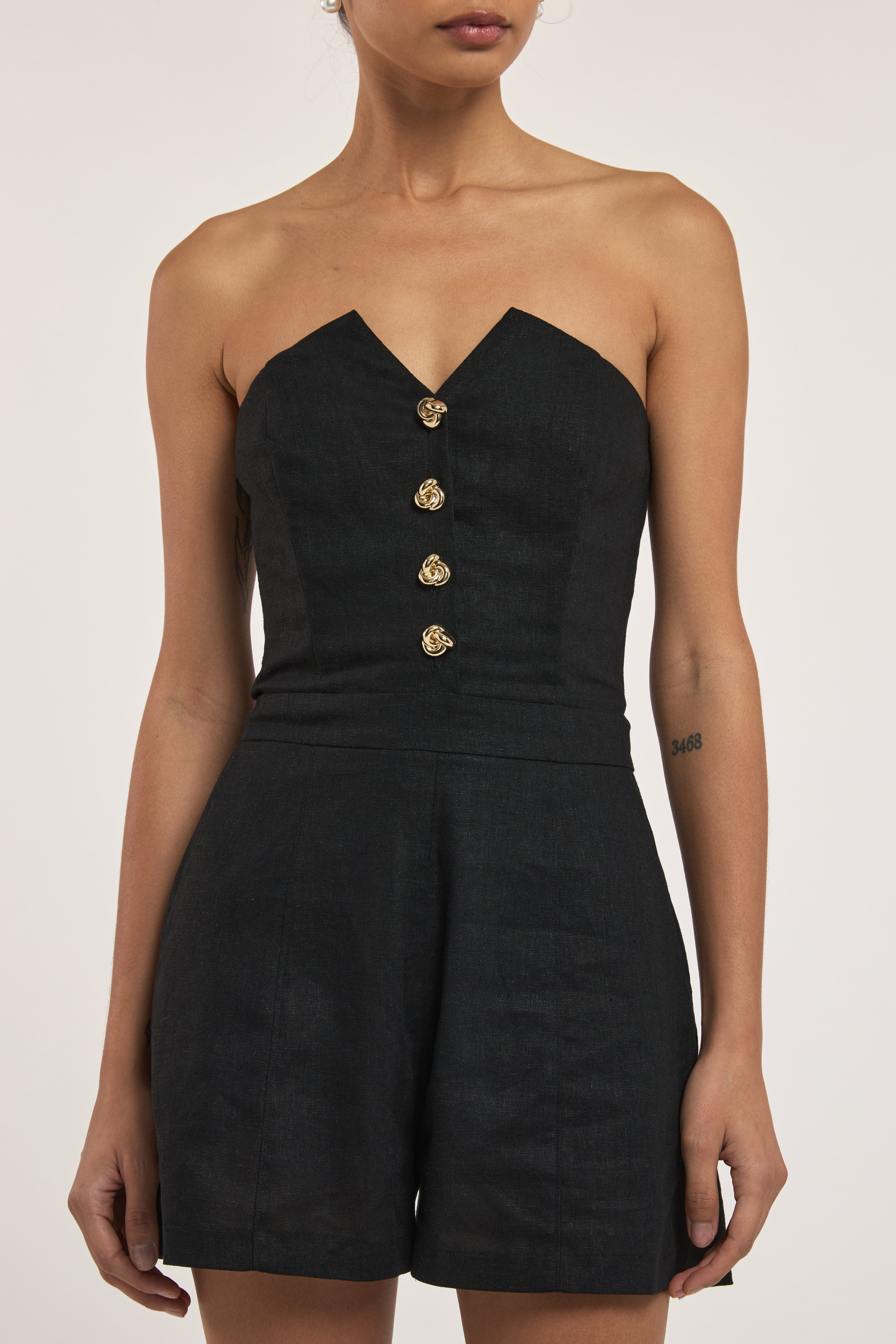 Black strapless romper with gold buttons on a white background